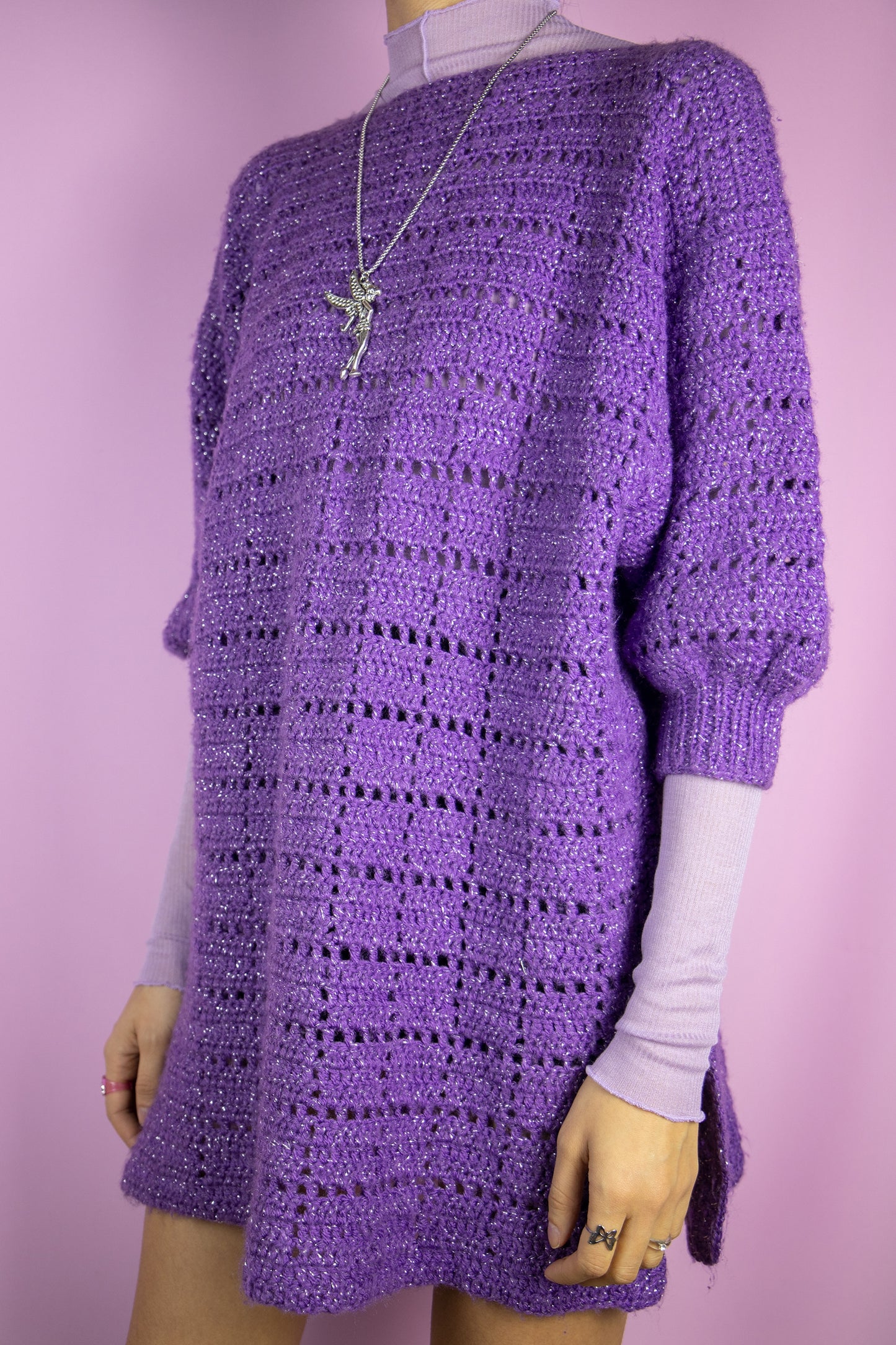 The Vintage 90s Purple Crochet Knit Sweater is a chunky, oversized-style short-sleeve pullover featuring intricate crochet patterns and sparkling silver thread details. Perfect for any casual or party outfit.