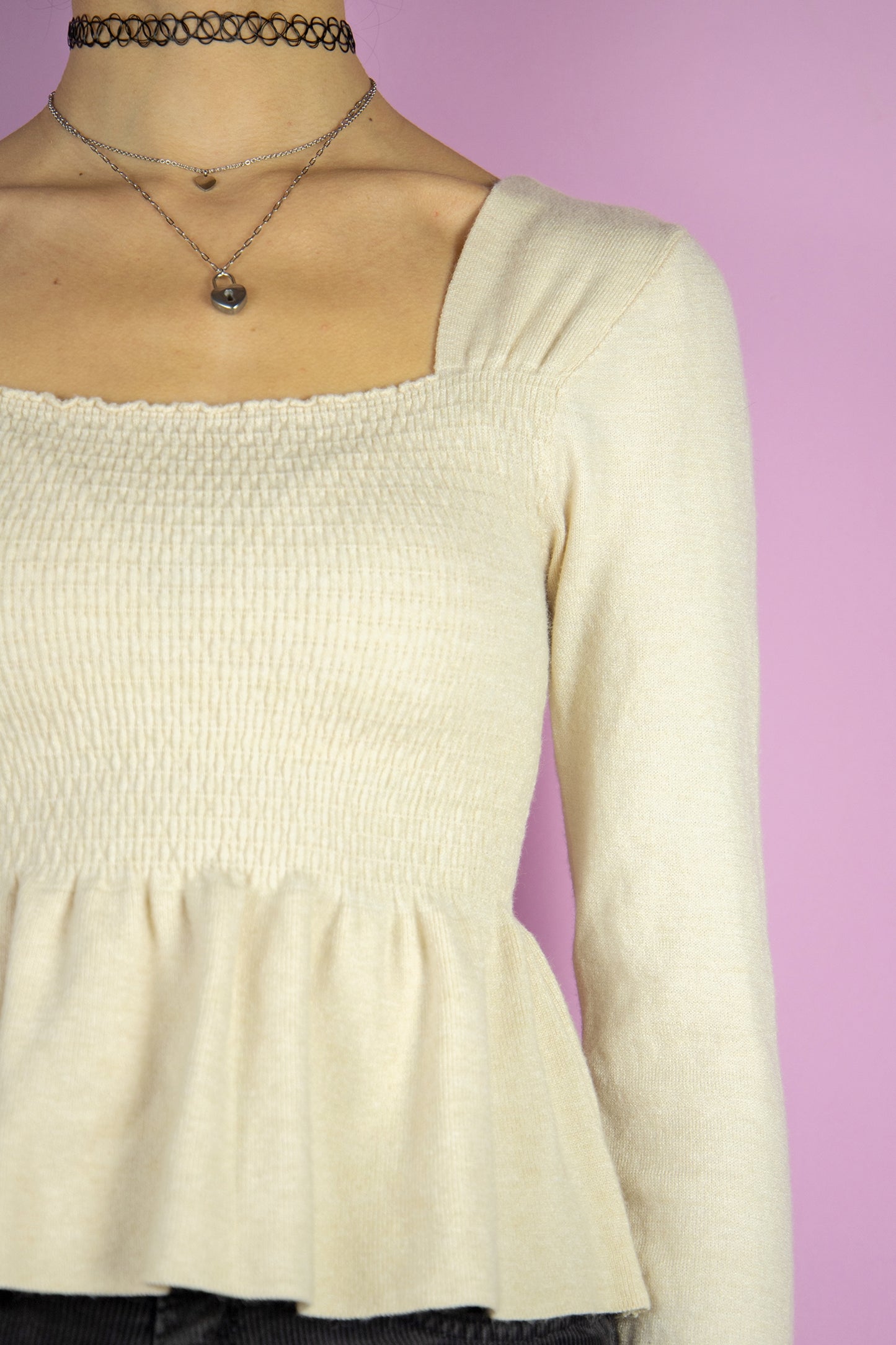 The Y2K Beige Shirred Peplum Top is a vintage 2000s knit blouse featuring a square neckline, long sleeves, and a shirred bodice that flows into a peplum hem.
