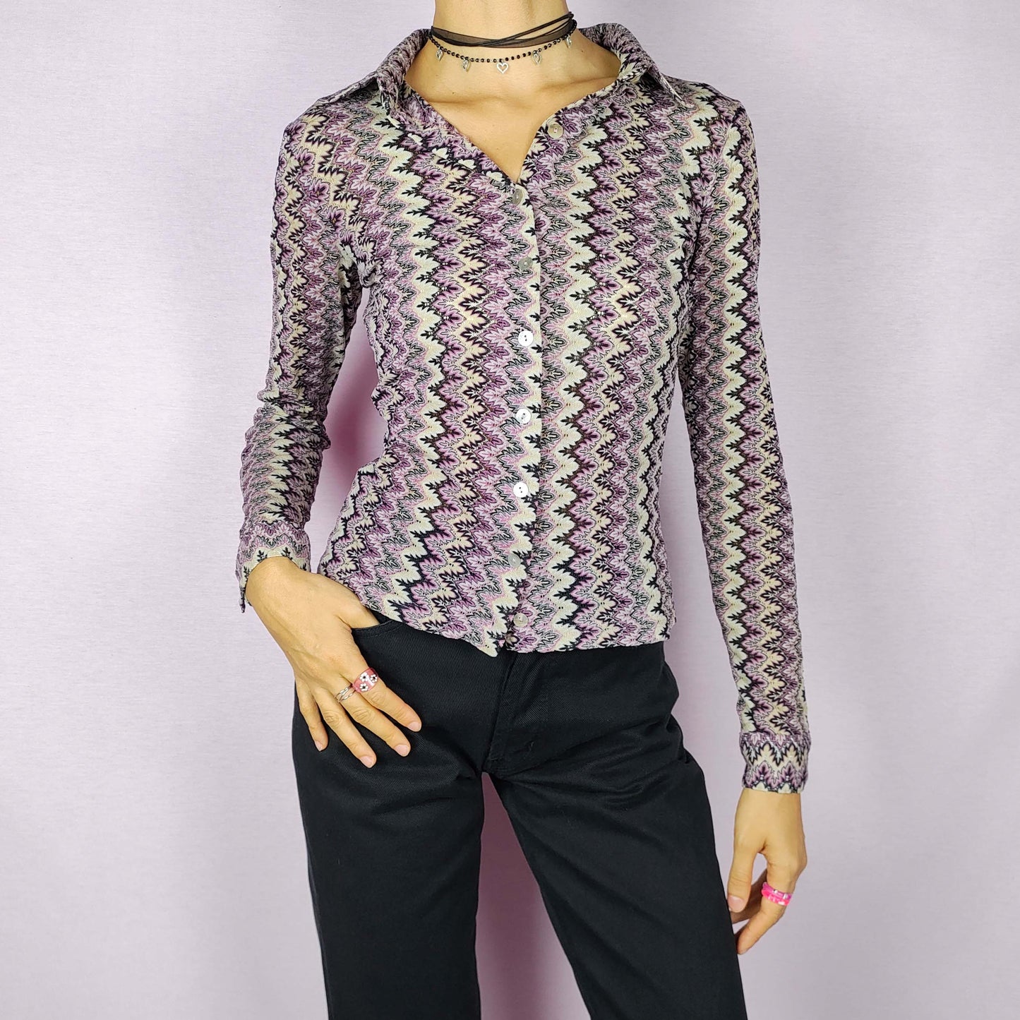 The Y2K Zigzag Mesh Top is a vintage 2000s shirt featuring a zigzag pattern in shades of black, pink, and beige. Made from a lightweight, stretchy mesh fabric, this button-up blouse offers a fitted silhouette with a pointed collar for a sleek look. Perfect for casual daytime wear.