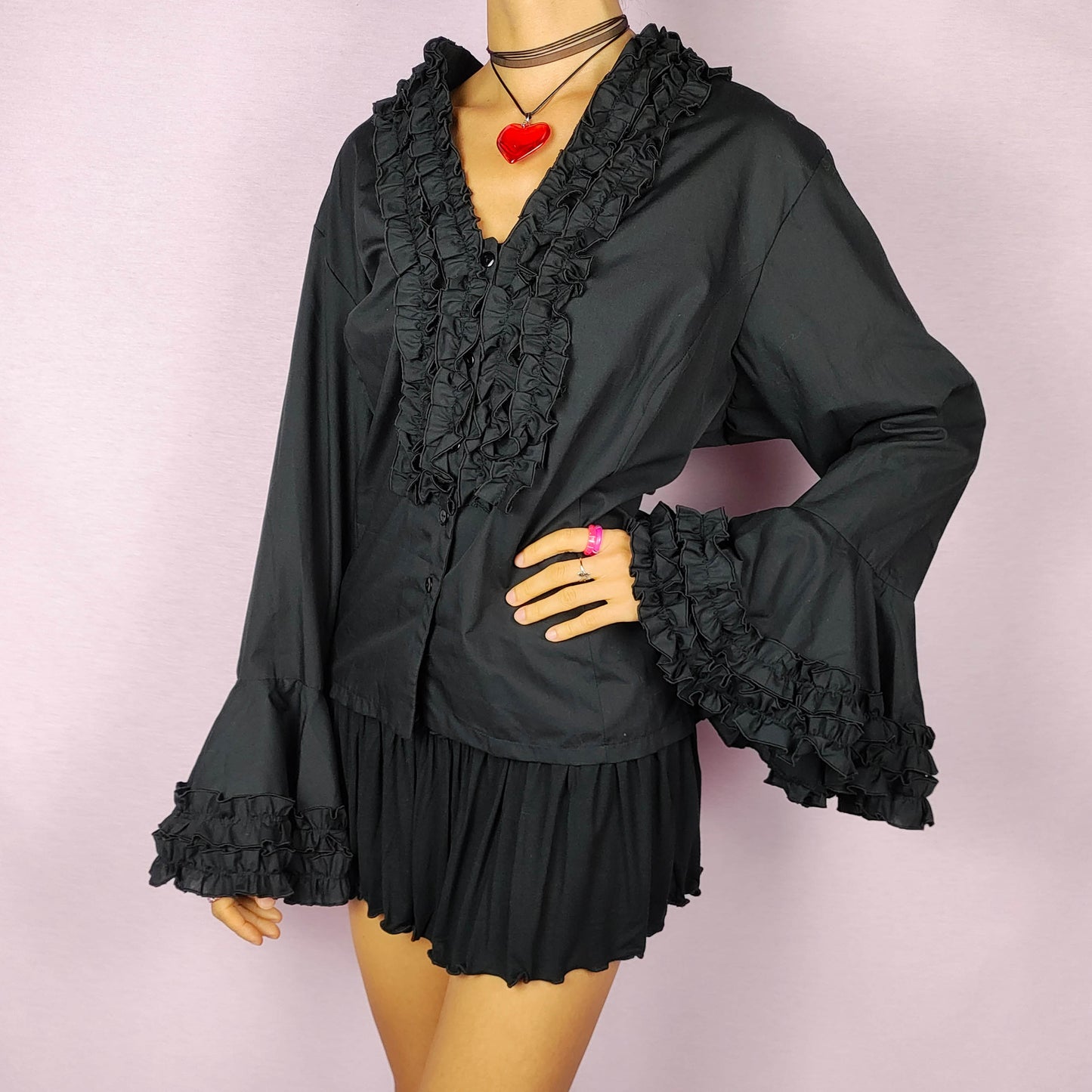 The Vintage 80s Black Ruffle Blouse is a statement shirt, featuring dramatic frill and ruffle detailing along the neckline and front button closure. This blouse includes voluminous bell sleeves with layered ruffles and frills. Perfect for a formal look or a night out.
