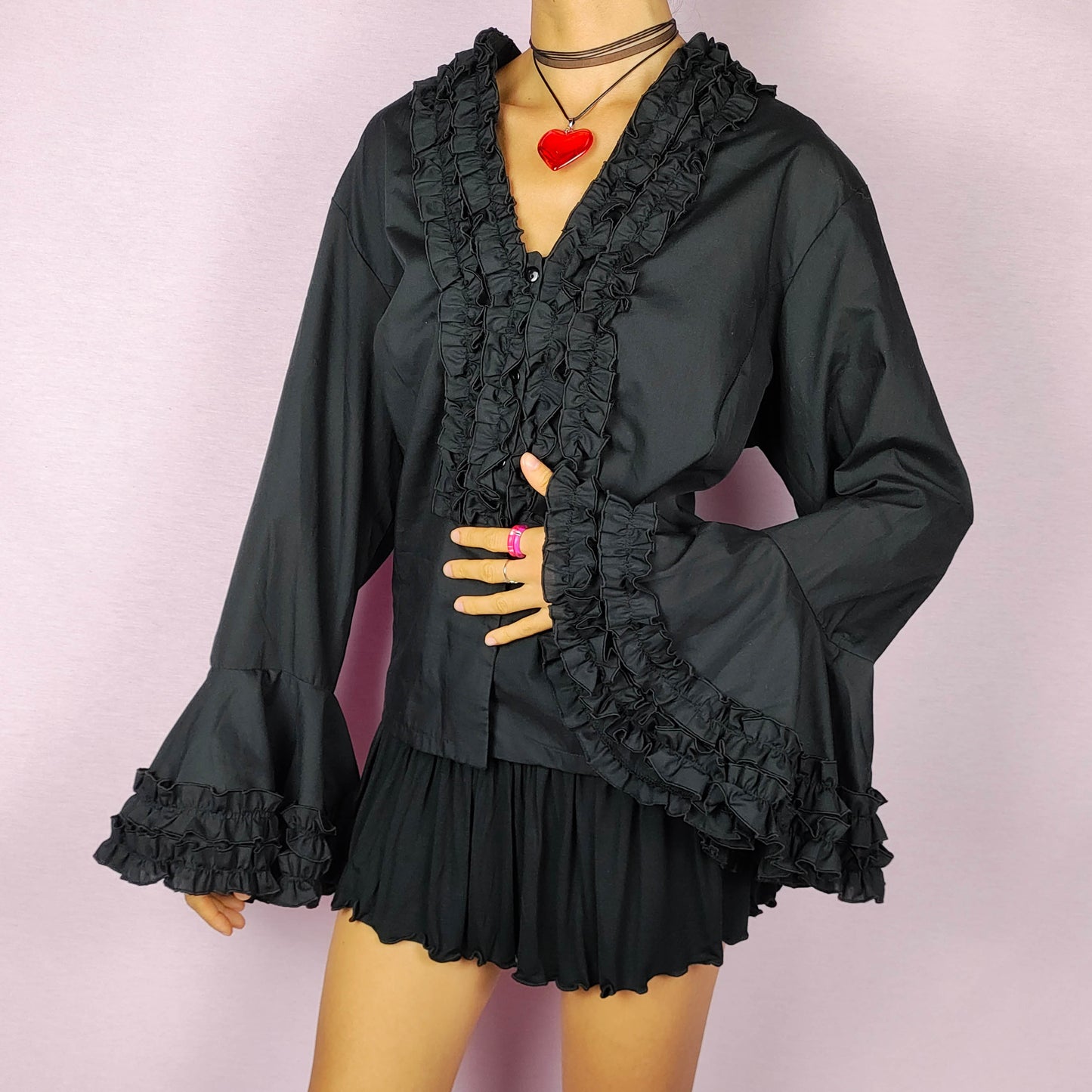 The Vintage 80s Black Ruffle Blouse is a statement shirt, featuring dramatic frill and ruffle detailing along the neckline and front button closure. This blouse includes voluminous bell sleeves with layered ruffles and frills. Perfect for a formal look or a night out.