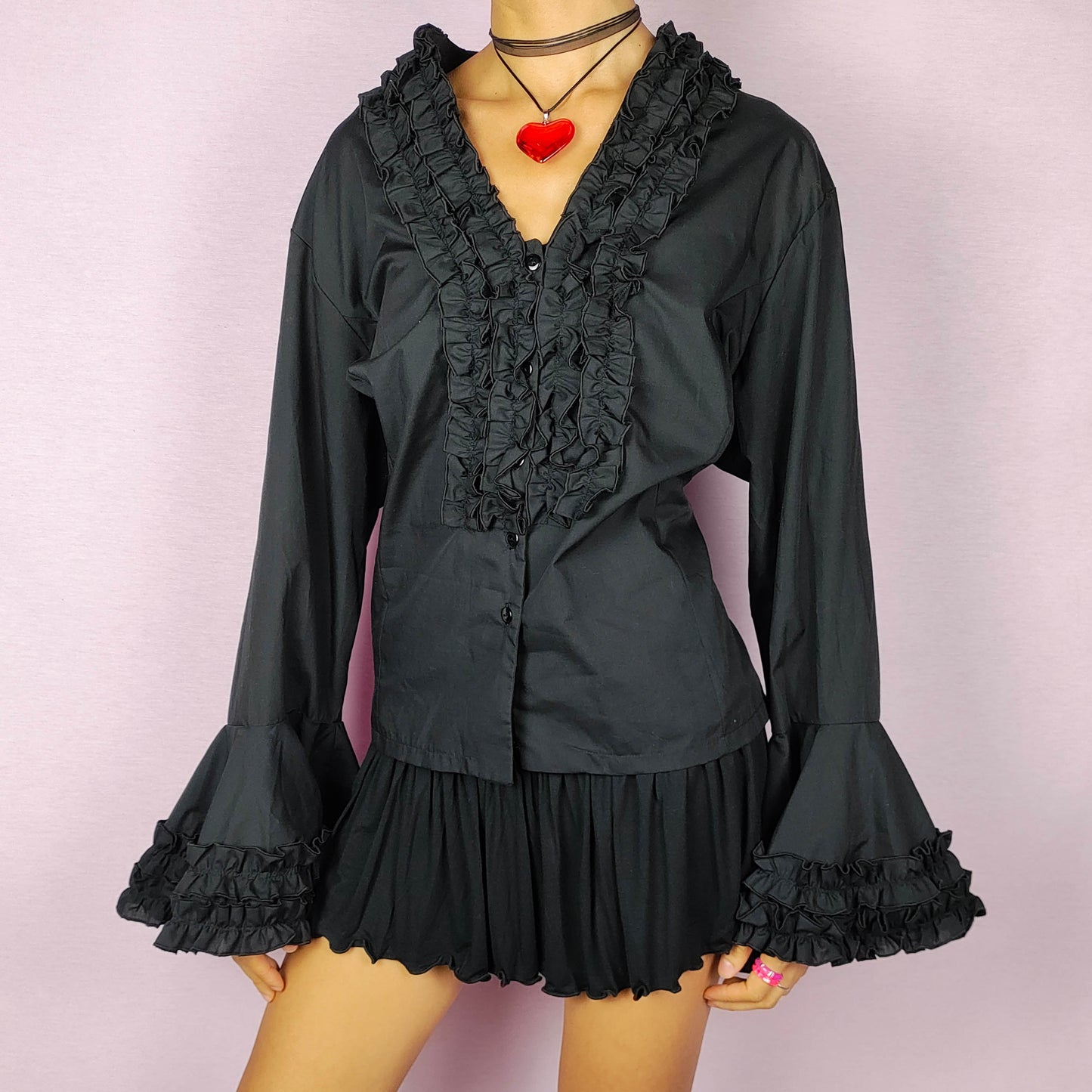 The Vintage 80s Black Ruffle Blouse is a statement shirt, featuring dramatic frill and ruffle detailing along the neckline and front button closure. This blouse includes voluminous bell sleeves with layered ruffles and frills. Perfect for a formal look or a night out.