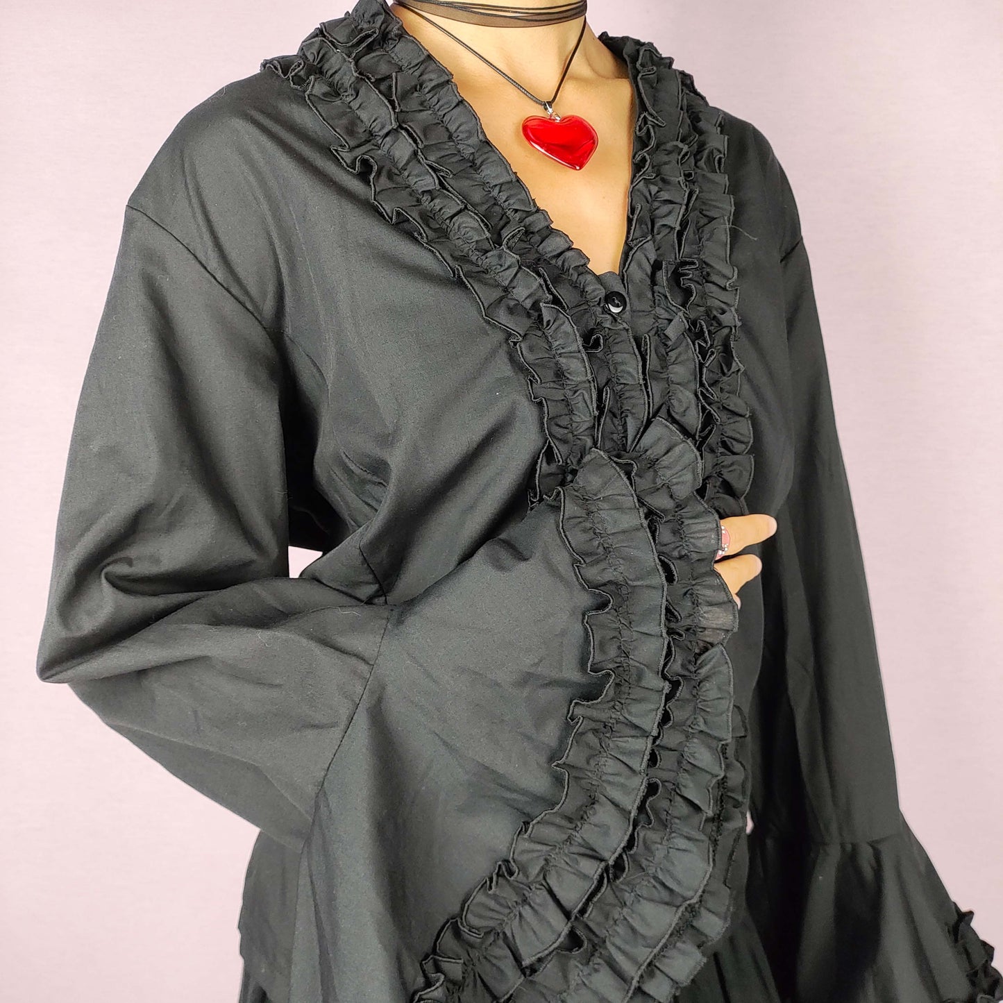 The Vintage 80s Black Ruffle Blouse is a statement shirt, featuring dramatic frill and ruffle detailing along the neckline and front button closure. This blouse includes voluminous bell sleeves with layered ruffles and frills. Perfect for a formal look or a night out.