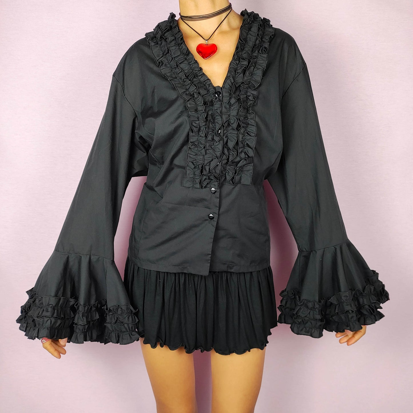 The Vintage 80s Black Ruffle Blouse is a statement shirt, featuring dramatic frill and ruffle detailing along the neckline and front button closure. This blouse includes voluminous bell sleeves with layered ruffles and frills. Perfect for a formal look or a night out.