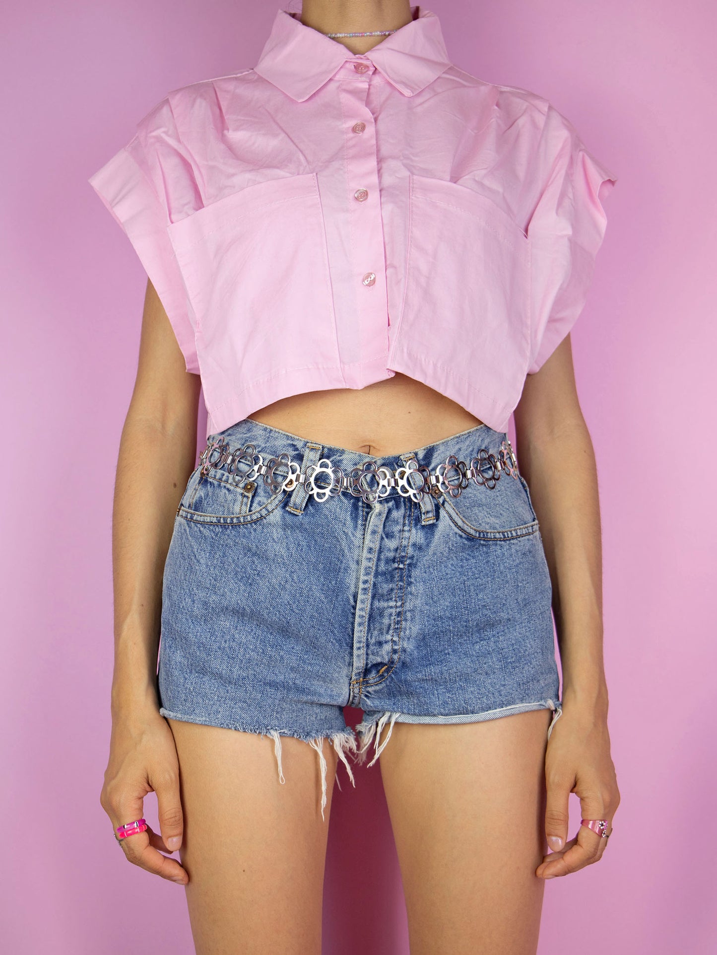 The Y2K Pink Sleeveless Crop Top is a vintage 2000s preppy school style cropped shirt featuring pleats, a collar, pastel pink color and pockets. Perfect for a casual summer outfit.