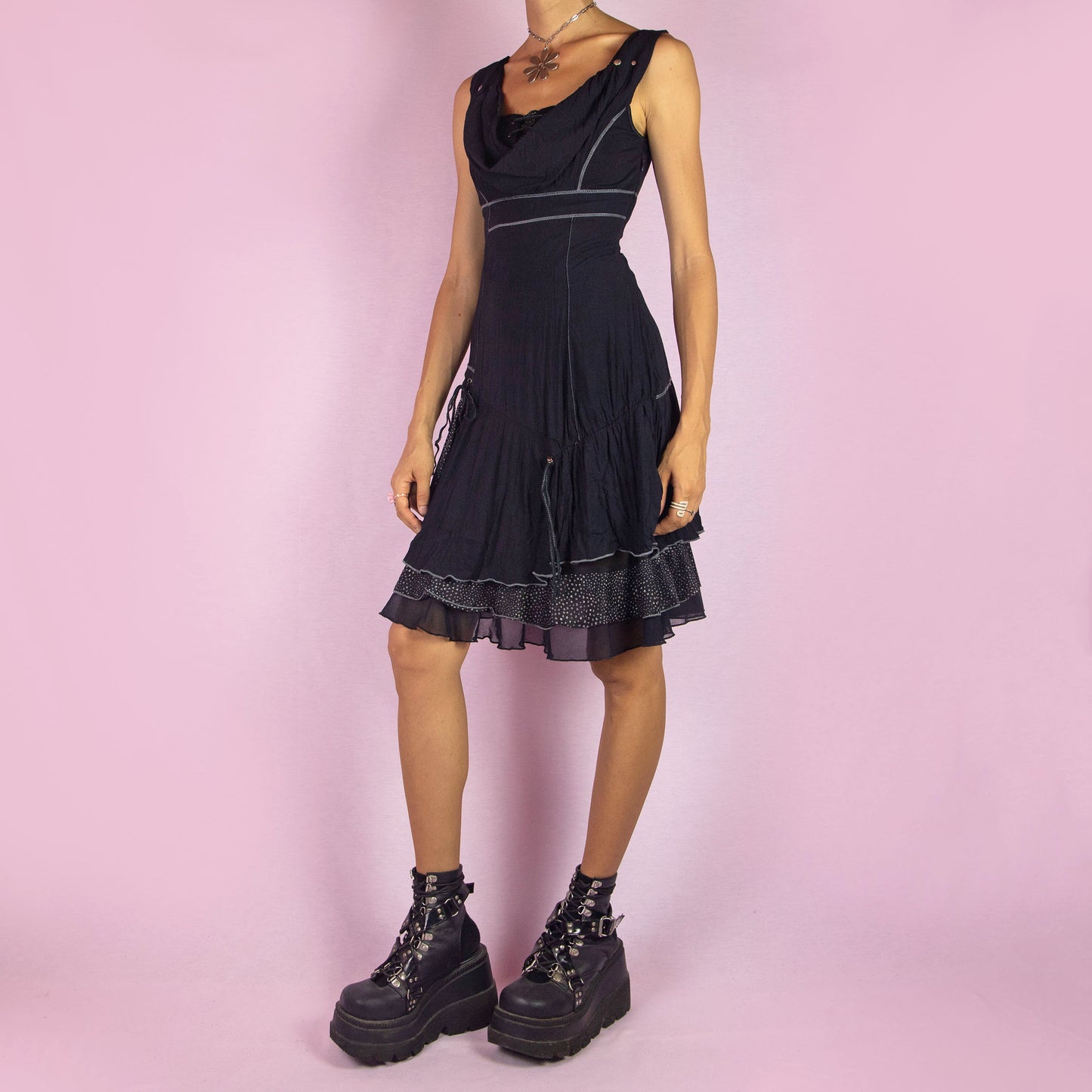 The Y2K Black Cowl Layered Dress is a vintage 2000s whimsy mini dress with a sleeveless design, stretchy fabric, a flattering cowl neckline, asymmetrical details, contrasting stitching, and lace-up accents. It also features a side zipper closure. Perfect for casual outings, evening events, or dressed up for a night out.
