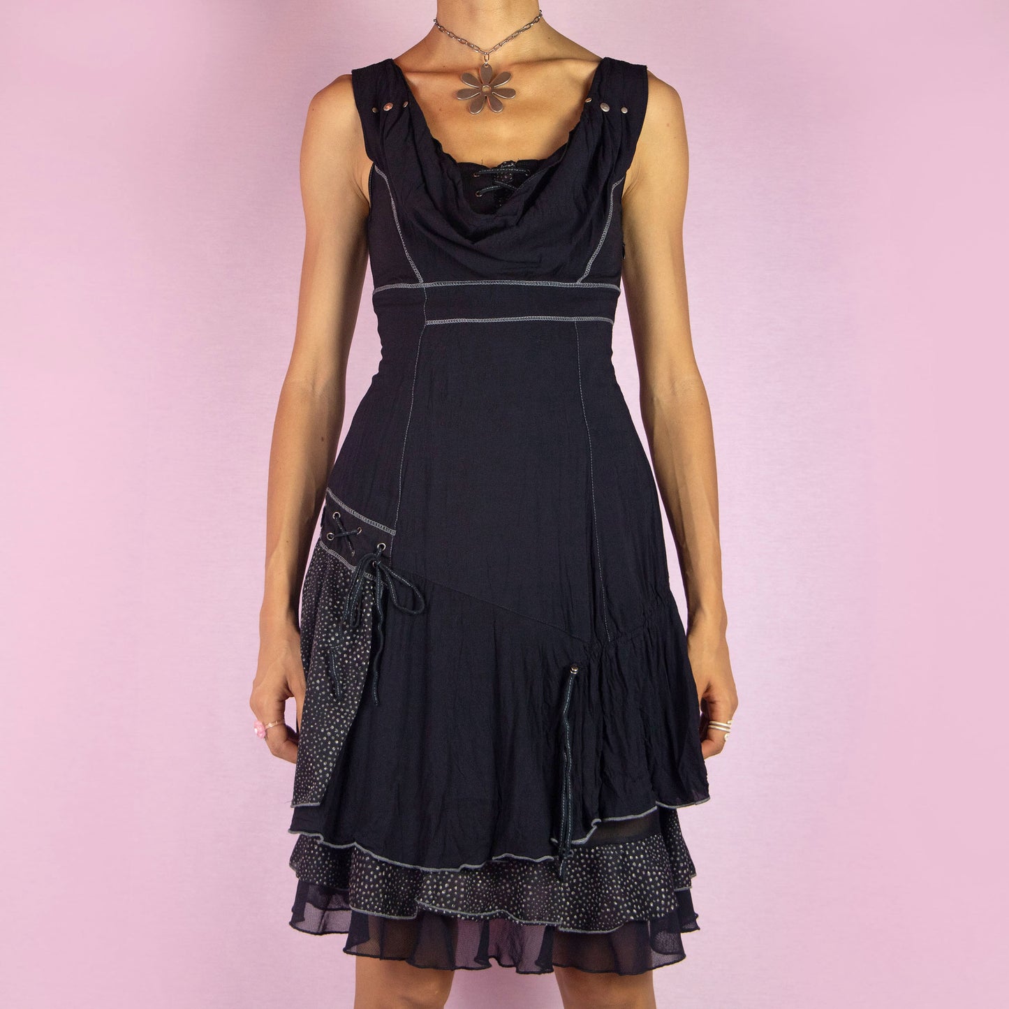 The Y2K Black Cowl Layered Dress is a vintage 2000s whimsy mini dress with a sleeveless design, stretchy fabric, a flattering cowl neckline, asymmetrical details, contrasting stitching, and lace-up accents. It also features a side zipper closure. Perfect for casual outings, evening events, or dressed up for a night out.