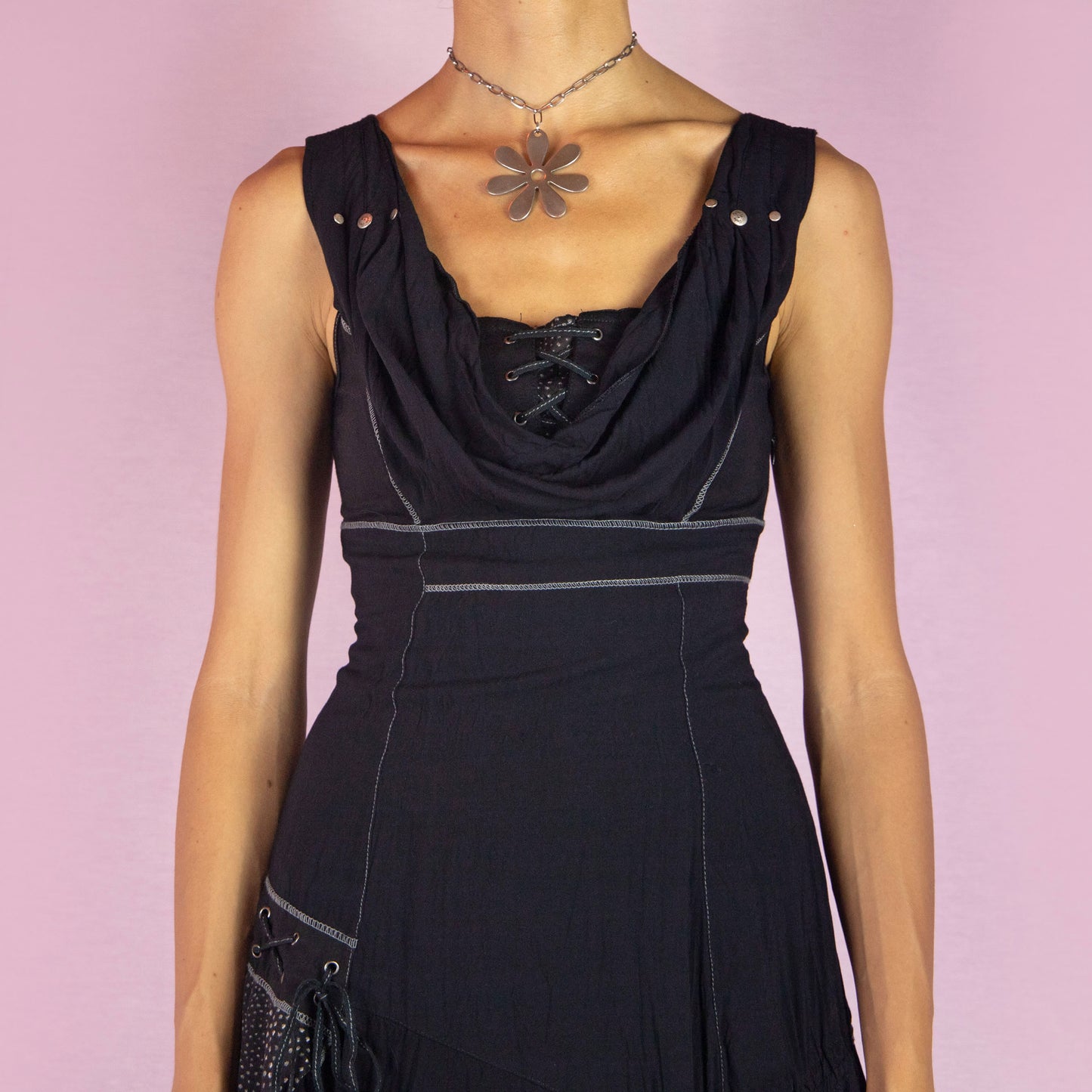 The Y2K Black Cowl Layered Dress is a vintage 2000s whimsy mini dress with a sleeveless design, stretchy fabric, a flattering cowl neckline, asymmetrical details, contrasting stitching, and lace-up accents. It also features a side zipper closure. Perfect for casual outings, evening events, or dressed up for a night out.