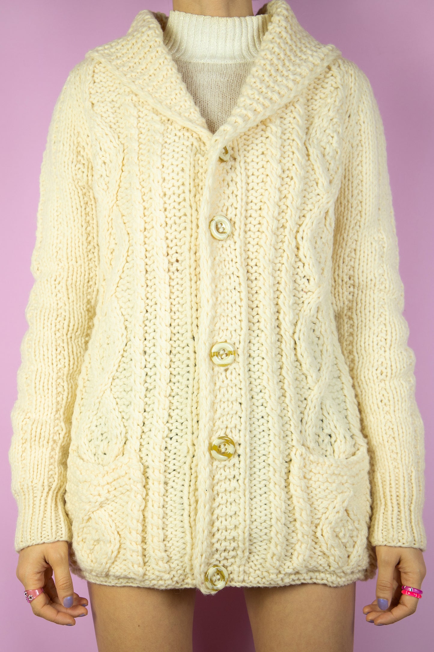 The Vintage 90s Beige Wool Knit Cardigan is a cozy, cream chunky hand-knit wool cardigan, featuring buttons, front pockets a classic cable knit design and an oversized shawl collar. Perfect for autumn and winter days.