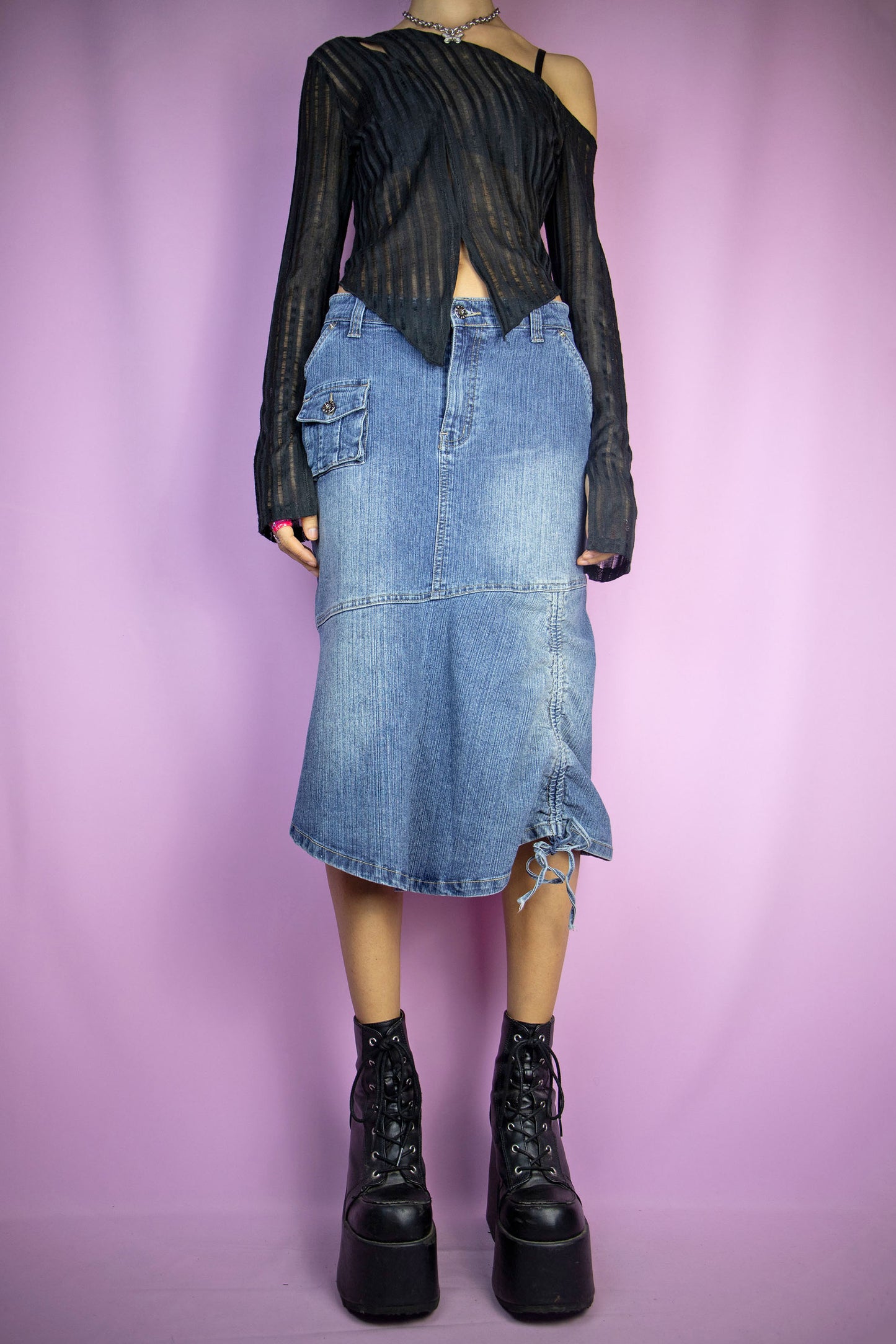 The Vintage Y2K Asymmetric Denim Midi Skirt is a stretch denim skirt featuring asymmetrical design, pockets, a flared hem, and a stylish ruched tie detail. This iconic deconstructed cyber jean maxi skirt captures the essence of the 2000s.