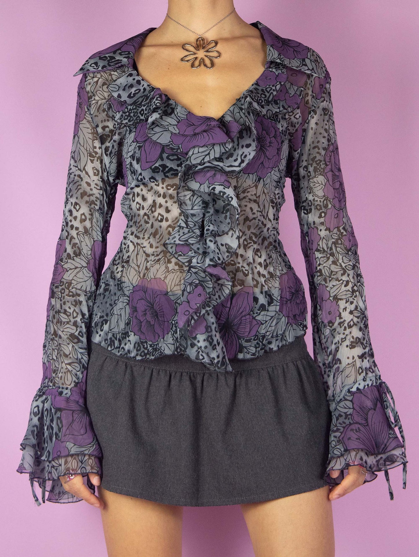 The Y2K Print Sheer Ruffle Blouse is a vintage 2000s top featuring a floral and leopard animal print, long bell sleeves, and a ruffle front. This semi-transparent blouse with frill details adds a touch of whimsy making it perfect for any statement outfit.