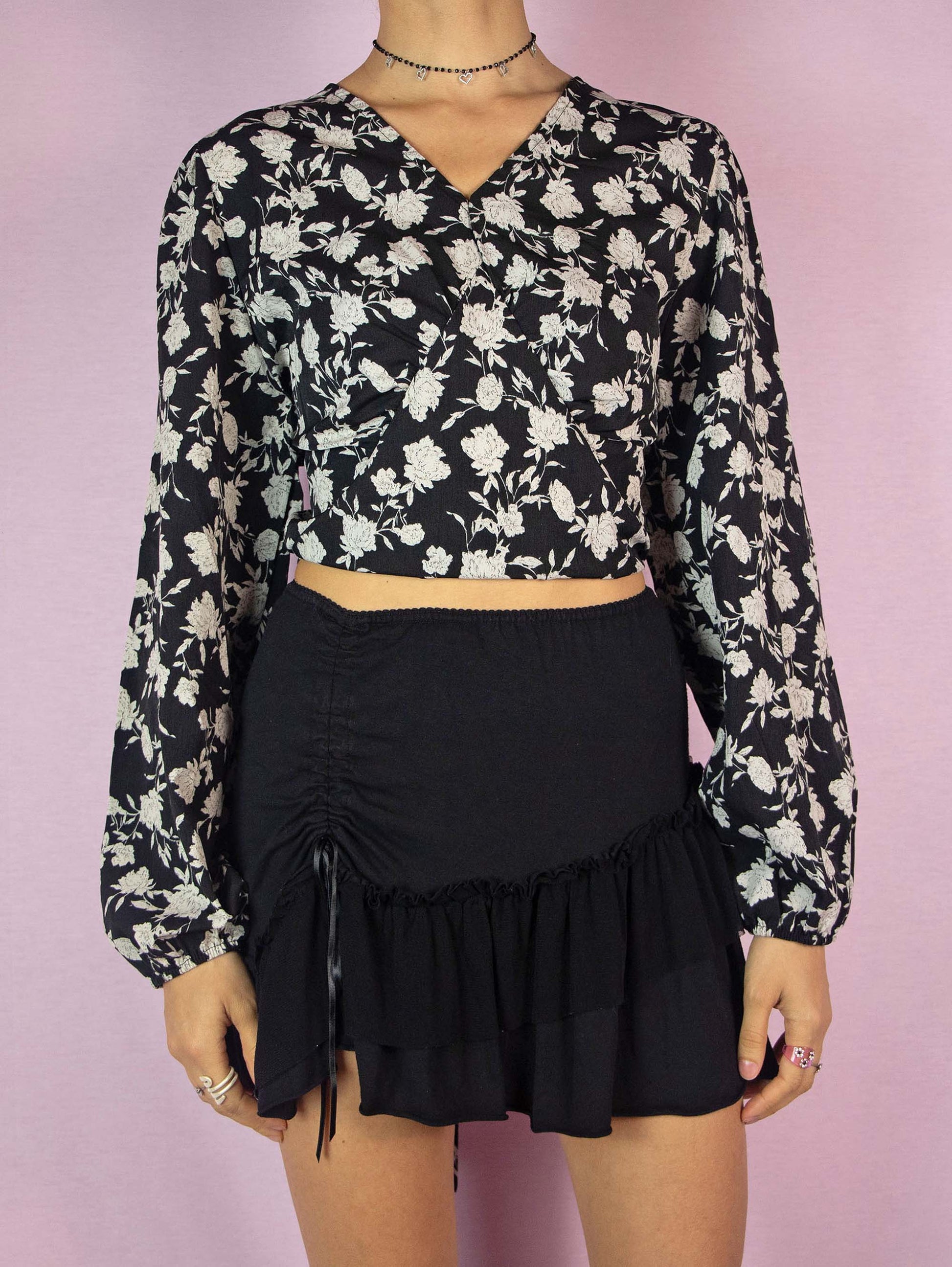 The Y2K Black Floral Tie Back Top is a vintage 2000s boho blouse with a floral graphic print, balloon sleeves, V-neckline, and elastic at the waist.