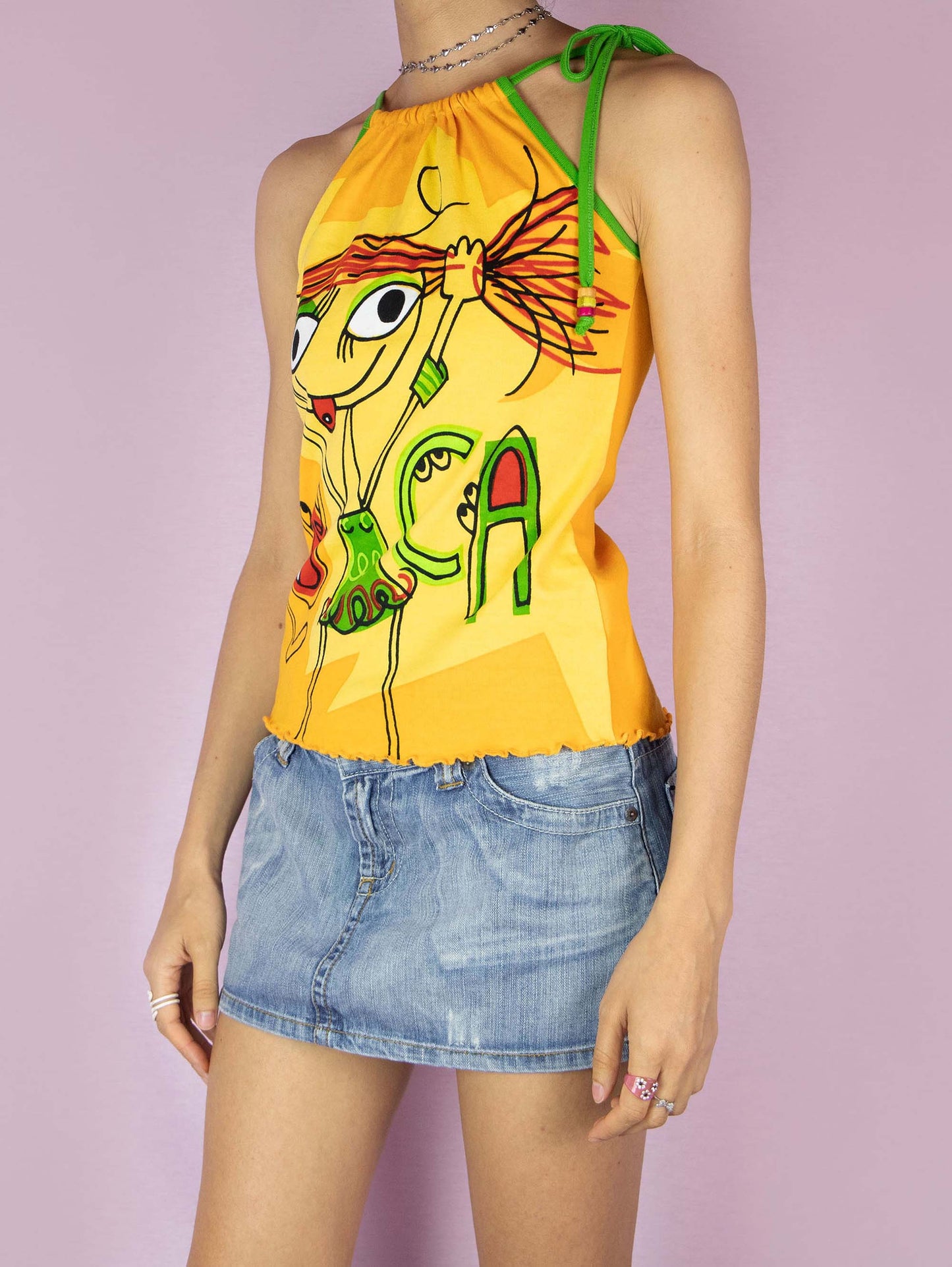 The Y2K Printed Sleeveless Top is a vintage 2000s yellow graphic halter top that features a vibrant cartoon design on the front, showcasing playful and colorful illustrations, making it perfect for a fun, casual summer look.