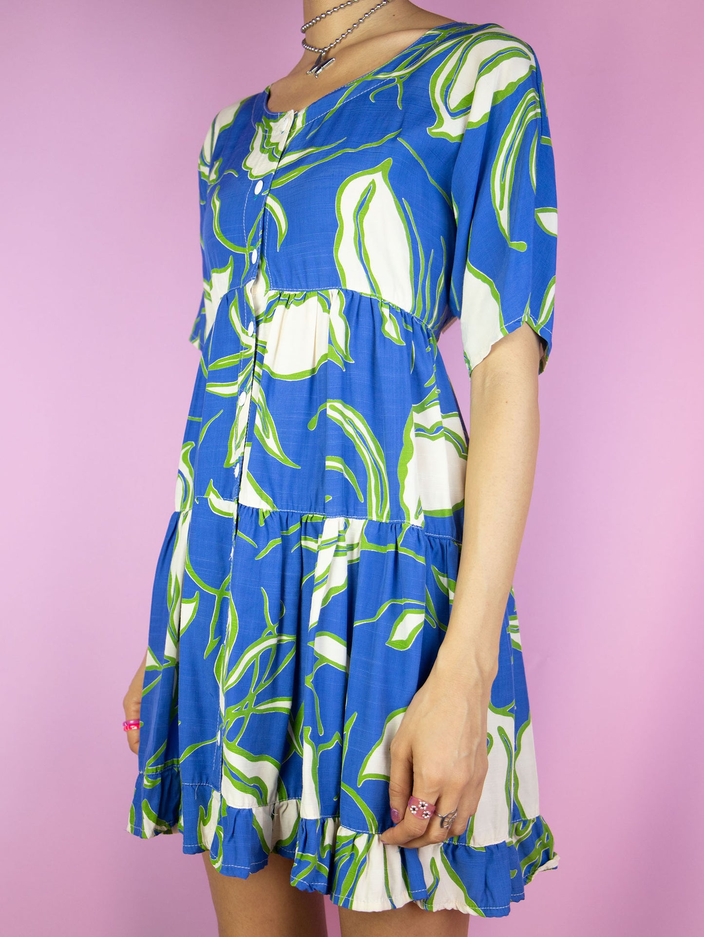 The Vintage 90s Floral Print Mini Dress is a boho summer beach style blue multicolored short sleeve tiered babydoll dress with buttons and a ruffle hem.