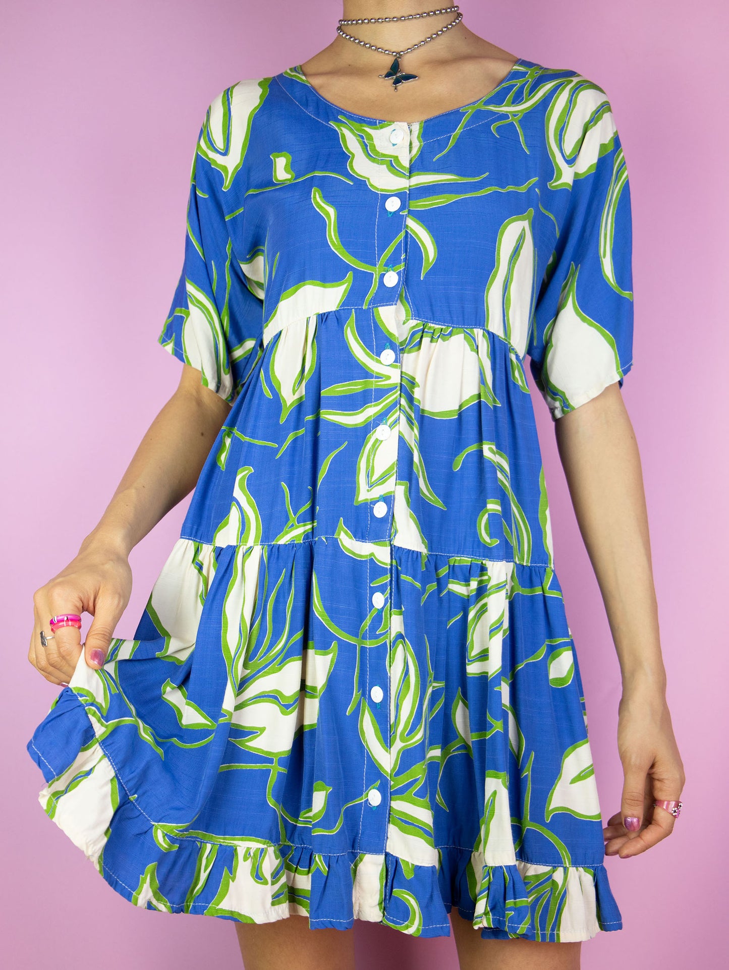 The Vintage 90s Floral Print Mini Dress is a boho summer beach style blue multicolored short sleeve tiered babydoll dress with buttons and a ruffle hem.