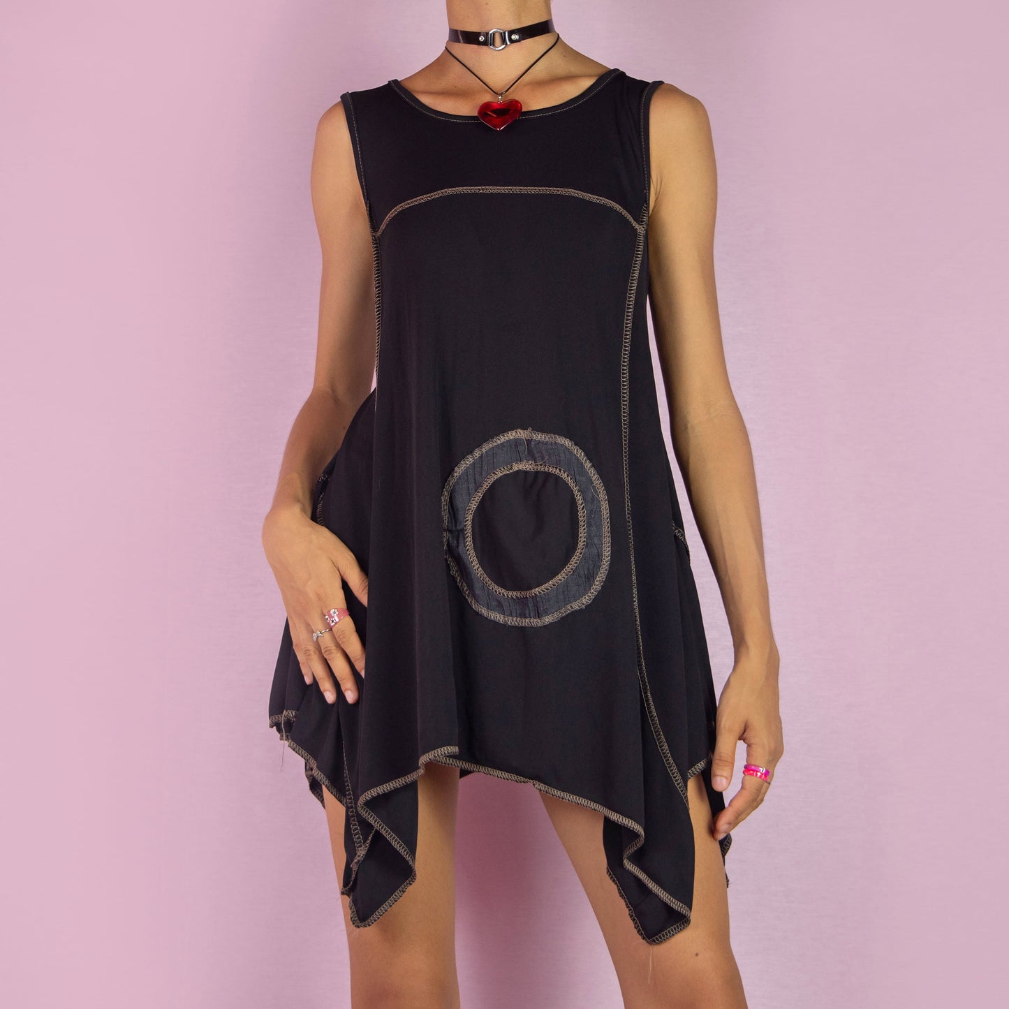 The Y2K Black Asymmetric Sleeveless Top is a vintage 2000s shirt featuring a flowy, oversized silhouette with bold circular stitched detailing. Made from stretchy fabric, this top has an asymmetric hemline, perfect for summer casual wear or layering for a unique, statement look. Made in Italy.