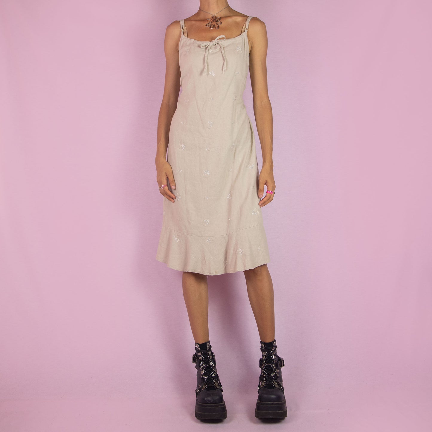 The Y2K Beige Linen Midi Dress is a vintage 2000s piece featuring a floral embroidery, tie-front detail, tie-back, and a back zipper closure. It also has adjustable spaghetti straps and a midi-length silhouette with a flared hem. Perfect for warm weather casual outings or a relaxed summer look.
