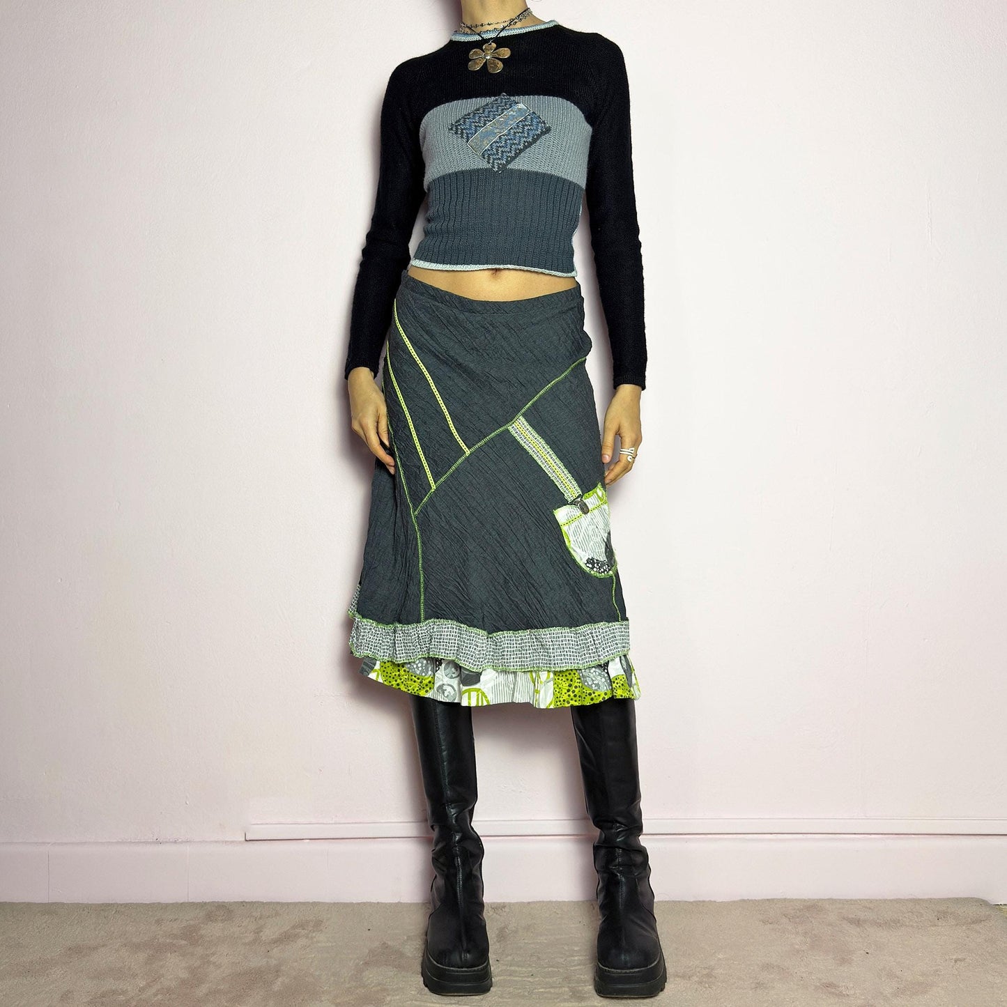 The Y2K Gray Patchwork Midi Skirt is a unique vintage 2000s piece featuring an eclectic mix of textures and contrasting neon green stitch details. Designed with a layered hem, ruffle trim, and a statement patch pocket with buckle detail, this skirt embodies a deconstructed boho aesthetic. The lightweight, crinkled fabric drapes effortlessly, while the elastic waistband ensures a comfortable fit, making it a perfect choice for bold, artsy outfits. Made in France. adult world shop