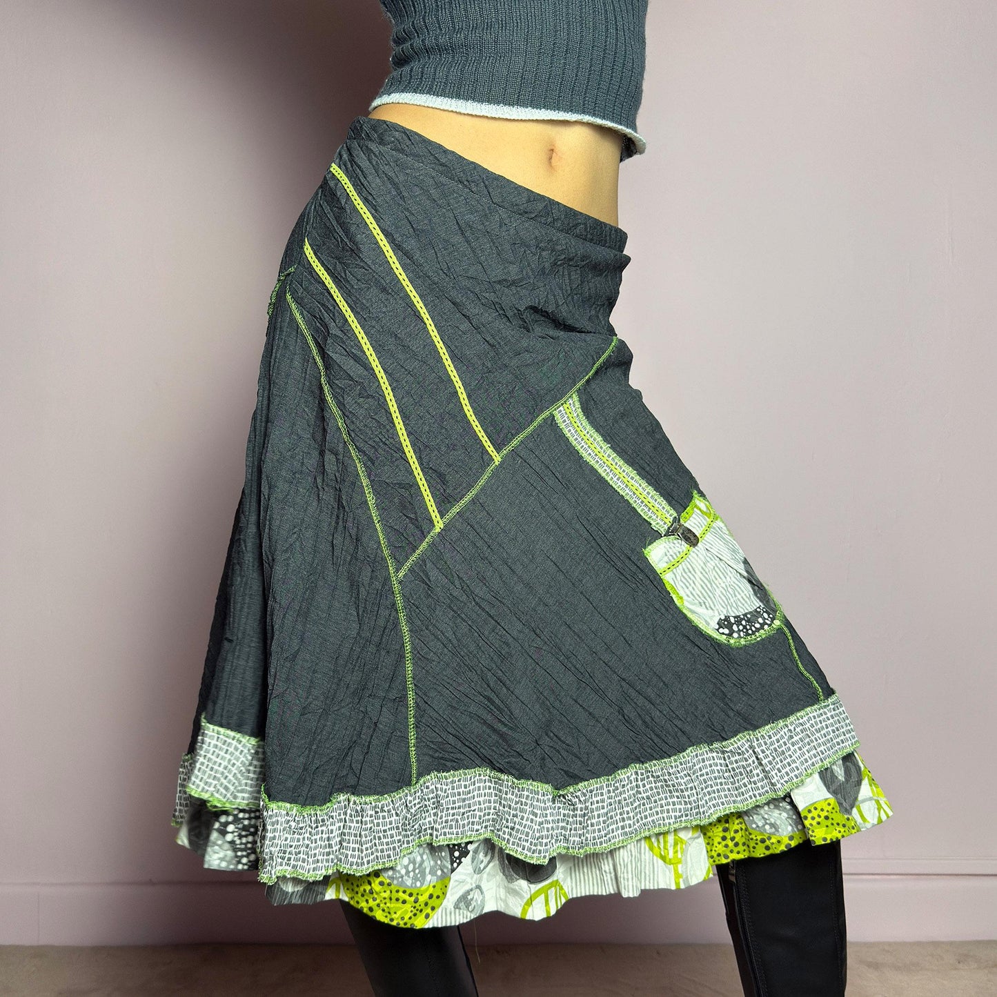 The Y2K Gray Patchwork Midi Skirt is a unique vintage 2000s piece featuring an eclectic mix of textures and contrasting neon green stitch details. Designed with a layered hem, ruffle trim, and a statement patch pocket with buckle detail, this skirt embodies a deconstructed boho aesthetic. The lightweight, crinkled fabric drapes effortlessly, while the elastic waistband ensures a comfortable fit, making it a perfect choice for bold, artsy outfits. Made in France. adult world shop