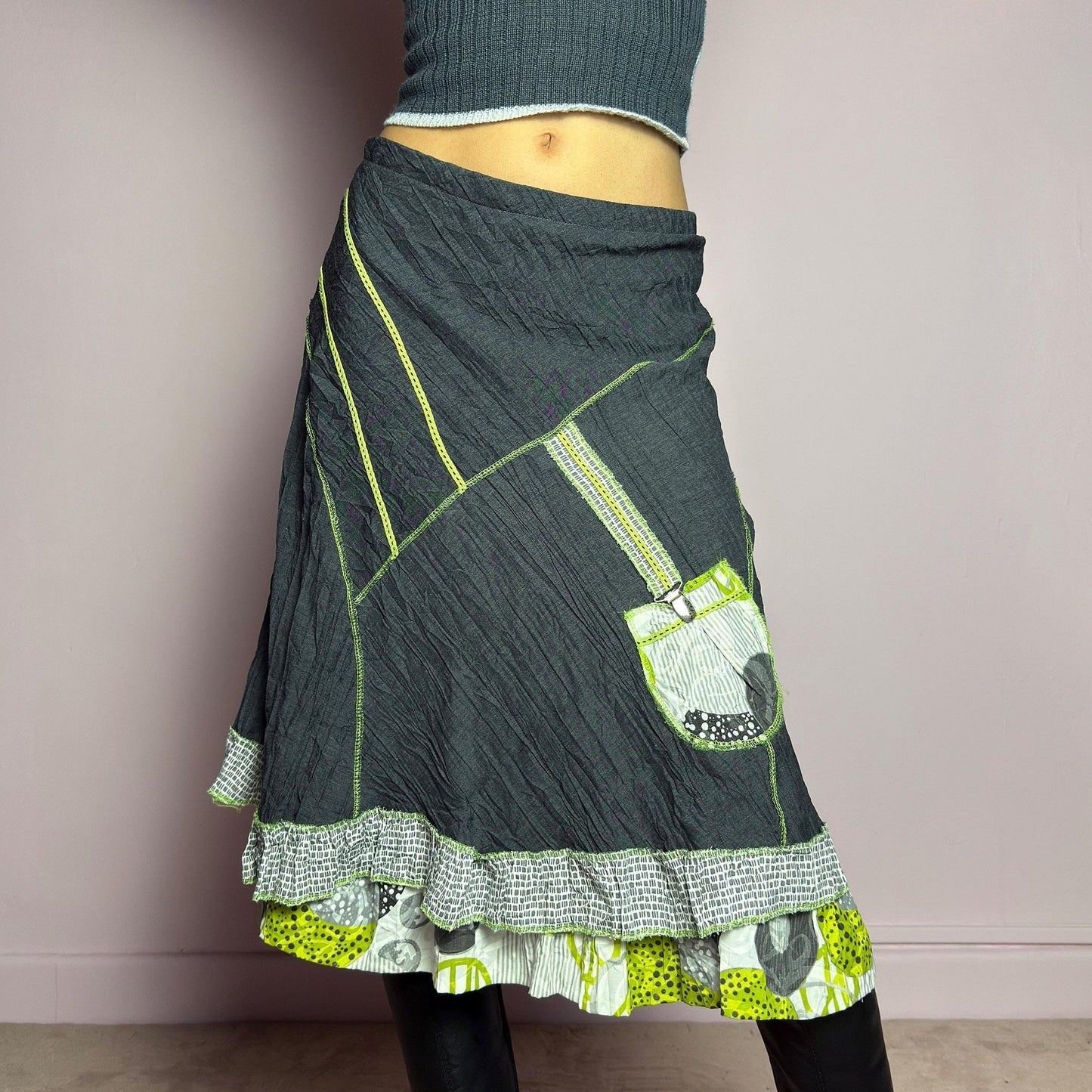 The Y2K Gray Patchwork Midi Skirt is a unique vintage 2000s piece featuring an eclectic mix of textures and contrasting neon green stitch details. Designed with a layered hem, ruffle trim, and a statement patch pocket with buckle detail, this skirt embodies a deconstructed boho aesthetic. The lightweight, crinkled fabric drapes effortlessly, while the elastic waistband ensures a comfortable fit, making it a perfect choice for bold, artsy outfits. Made in France. adult world shop