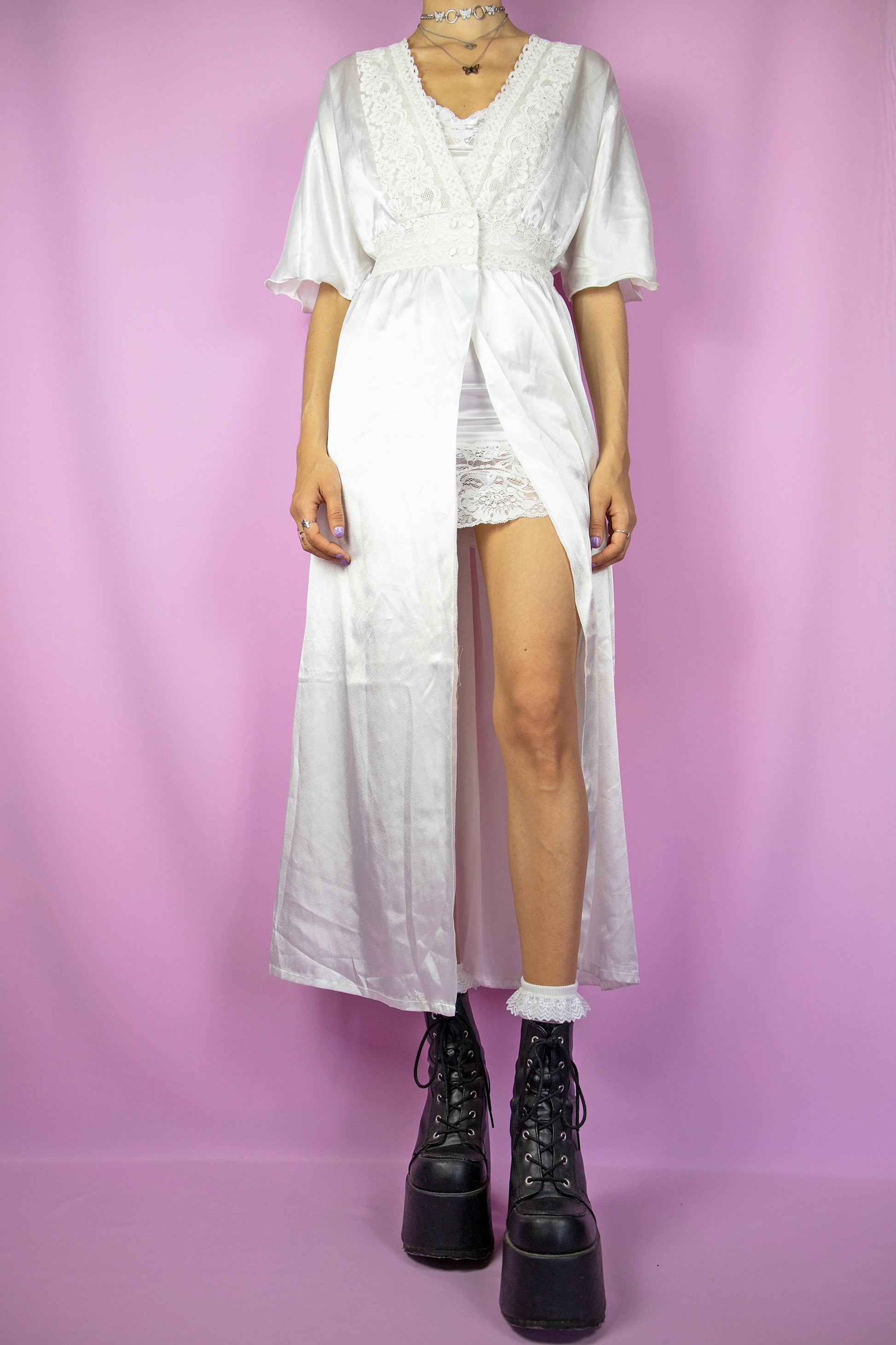 The Vintage 90s White Satin Duster Jacket is a white short-sleeved maxi duster coat with a button closure at the waist and lace details. Romantic 1990s white lace peignoir robe.