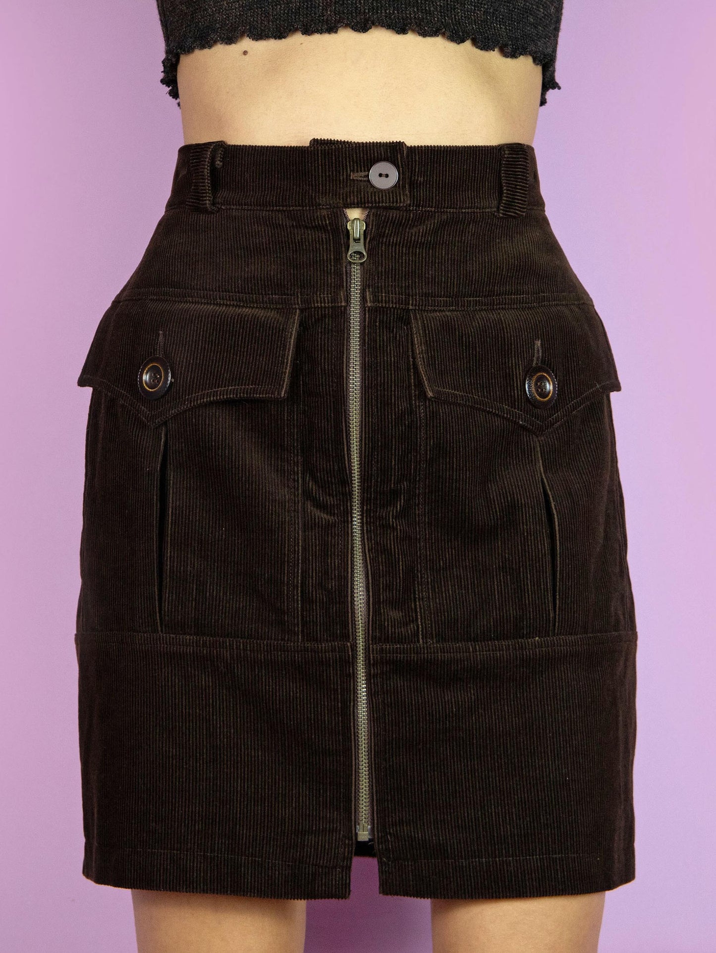 The Vintage 90s Brown Cargo Mini Skirt is a dark brown pencil corduroy skirt with pockets and a front zipper closure. Retro grunge 1990s utility mini skirt.