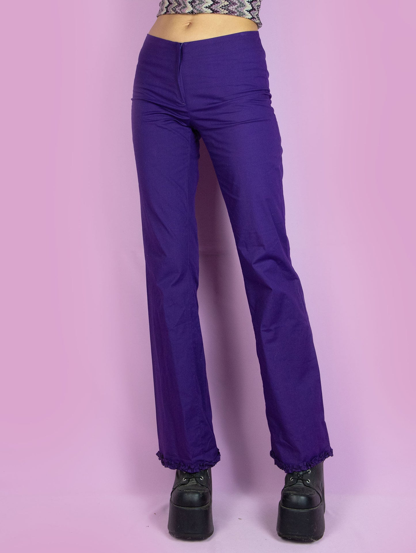 The Vintage 90s Dark Purple Flare Pants are mid-rise purple pants, slightly elastic and flared, with a front zipper closure and a gathered ruffle detail at the hem. Boho retro 1990s trousers.