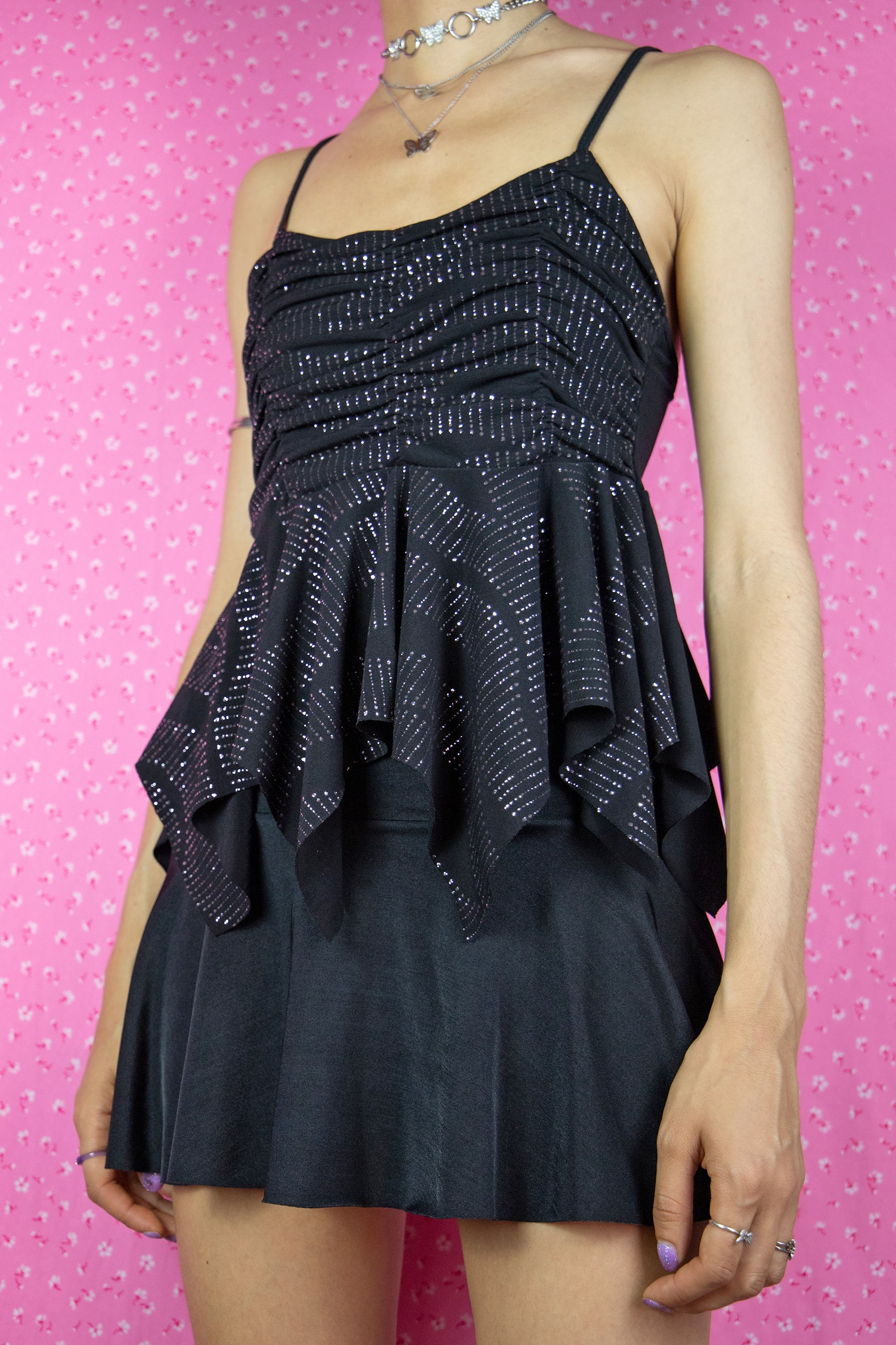 The Vintage Y2K Black Glitter Ruched Top is a sleek, pointy, stretch tank top in black with a ruched front and eye-catching sparkly glitter details. This stunning top perfectly embodies the cyber fairy goth Y2K style from the 2000s, making it a gorgeous addition to your collection.
