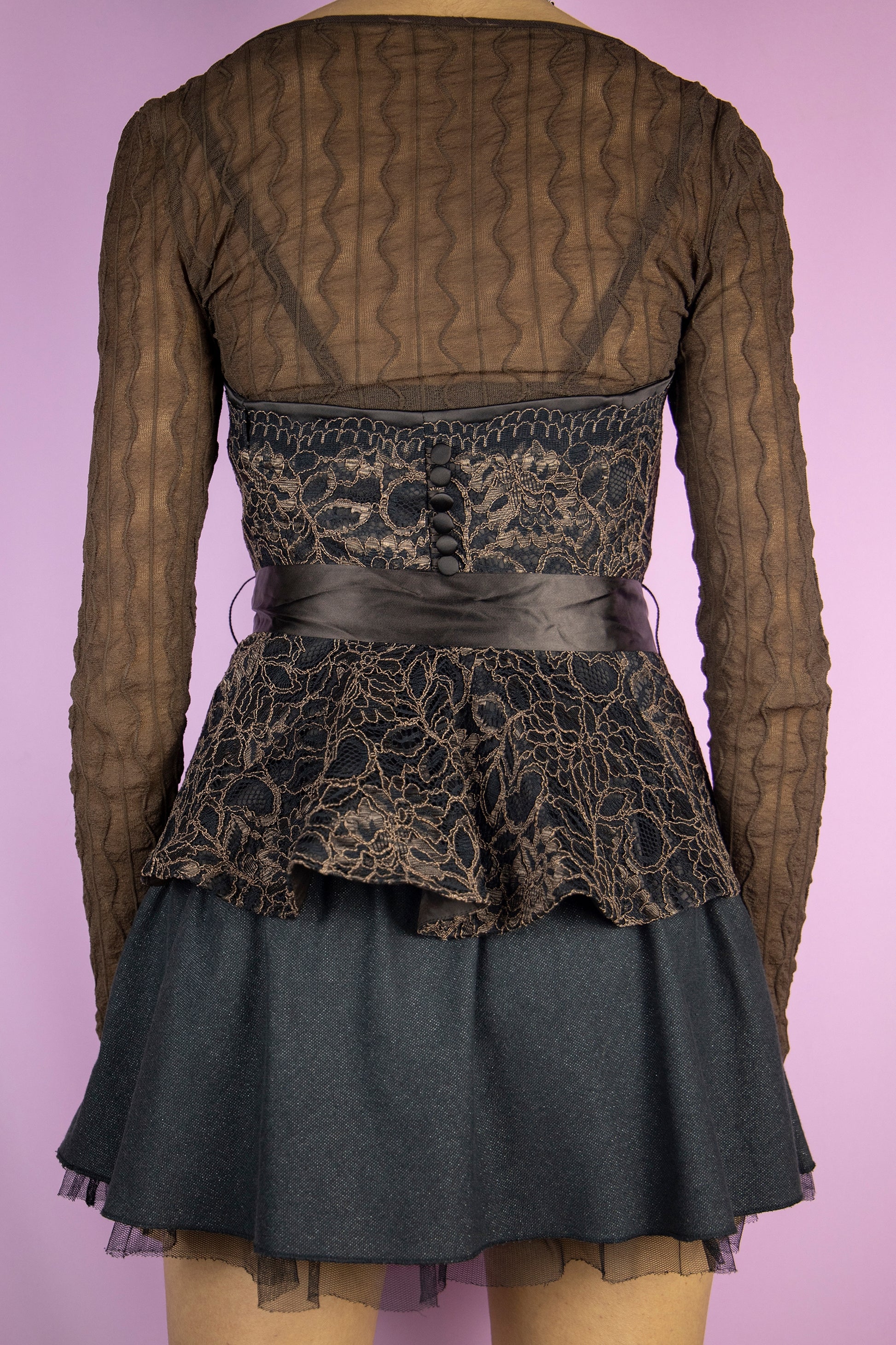 The Y2K Brown Lace Corset Top is a vintage brown and black strapless lace top with boning, buttons at the back, side zipper closure, and a ribbon that ties like a bow. Elegant fairy goth 2000s party night bustier. </span>The brown long-sleeved top shown underneath is not included.