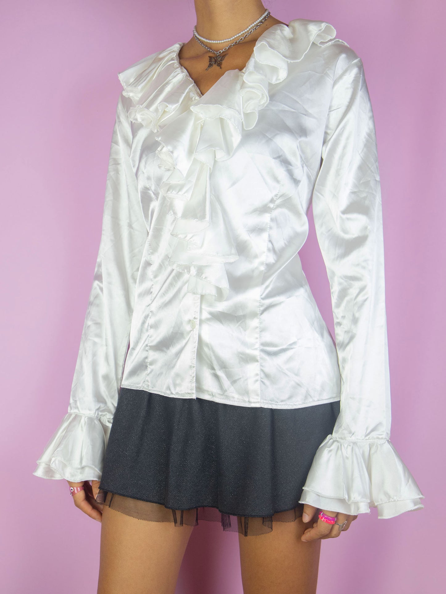 The Vintage 90s White Satin Ruffle Blouse is a shiny satin-style top with a ruffled collar, buttons, and bell sleeves. Romantic elegant 1990s evening party shirt.