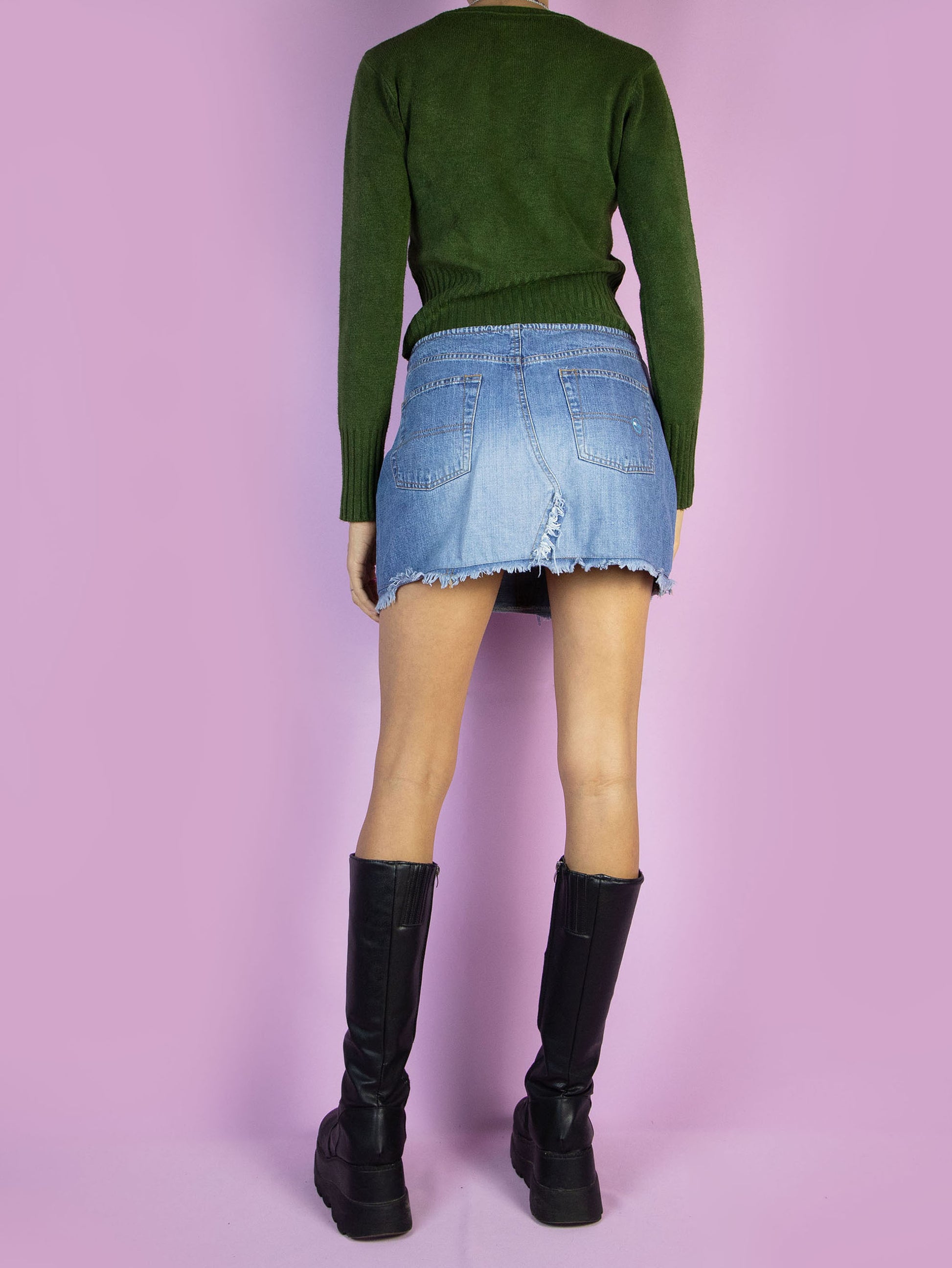 The Y2K Low Waisted Denim Mini Skirt is a vintage 2000s cyber grunge style low-rise jean mini skirt with pockets, a front zipper closure, and frayed details.
