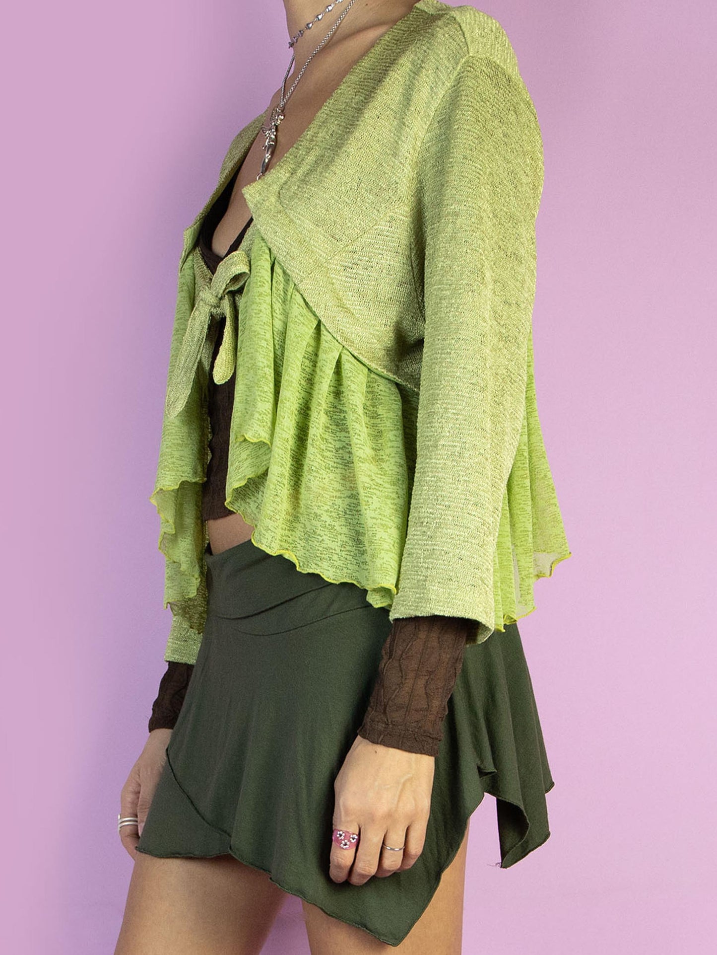 The Y2K Green Tie Bolero Jacket is a vintage three-quarter sleeve top that ties at the front and features a semi-sheer mesh ruffle detail. Boho fairy 2000s avant garde knit shrug.