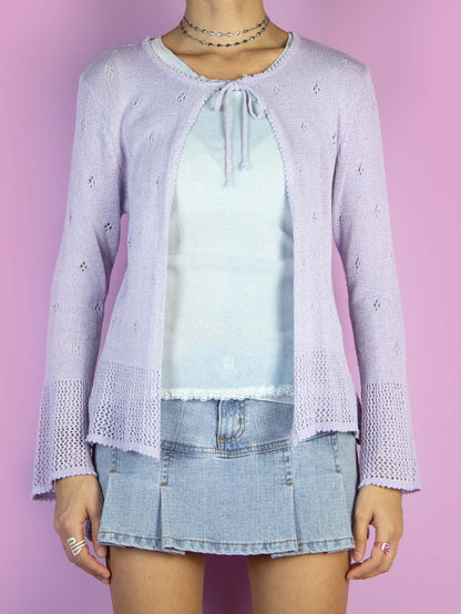 The Y2K Lilac Tie Front Cardigan is a light pastel purple cardigan that ties at the front and features bell sleeves. Cyber fairy grunge 2000s coquette crochet knit bolero jacket.