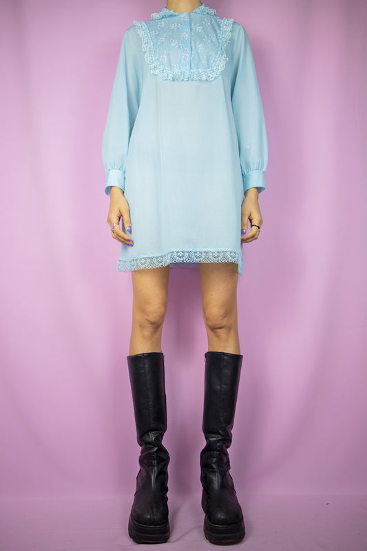 The Vintage 80’s Blue Ruffle Mini Dress is a charming light pastel blue, long-sleeved dress featuring buttons, a collar, intricate ruffles, and delicate lace details. This dress beautifully represents the classic retro style and the cottage prairie inspiration of the 1980s.