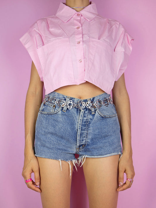 The Vintage Y2K Pink Crop Shirt is a sleeveless pastel light pink crop top, complete with pleats, pockets, a collar, and button detailing. This lovely piece embodies a preppy dress shirt style from the 2000s, making it an appealing addition to your wardrobe.