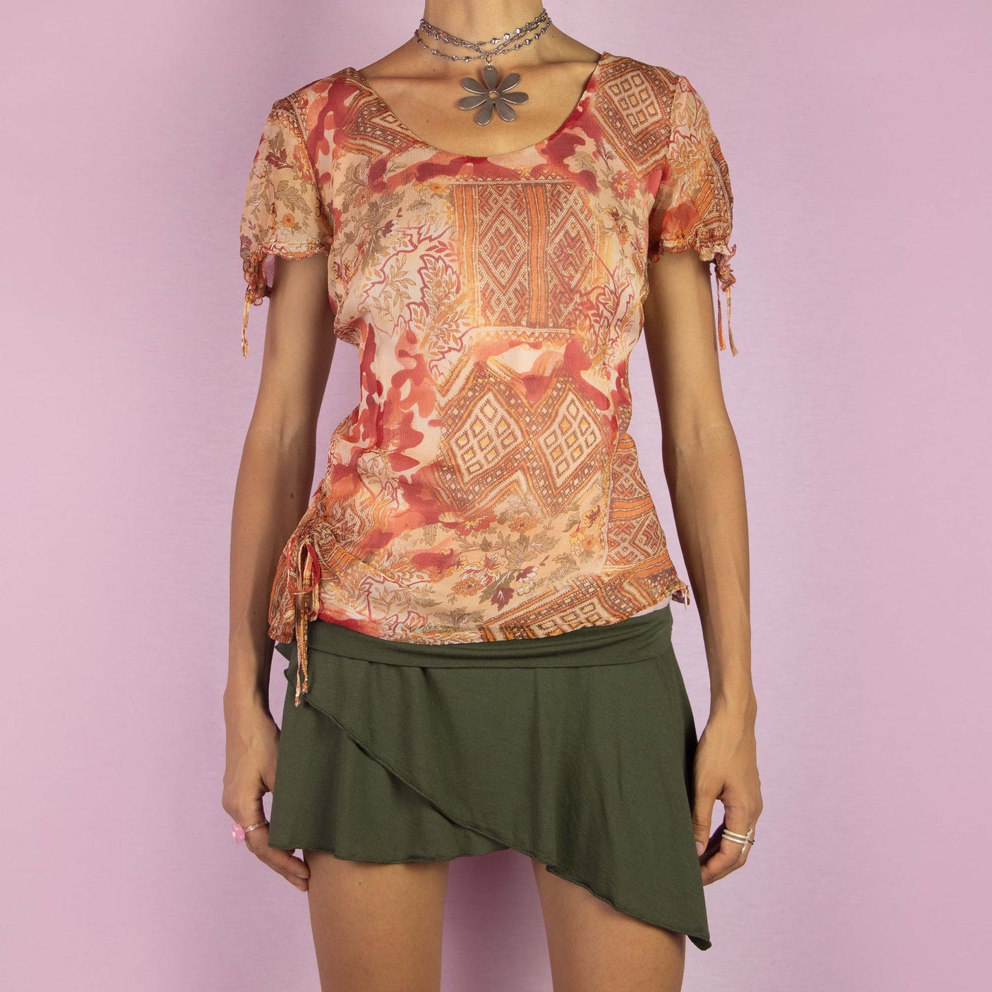 The Y2K Abstract Sheer Top is a vintage 2000s blouse featuring a warm-toned abstract print in orange, red and beige hues. Designed with a semi-sheer fabric overlay, short sleeves, adjustable side ruching with ties for a customized fit and a side zipper closure. Perfect for casual summer outings or adding a touch of boho flair to your wardrobe.