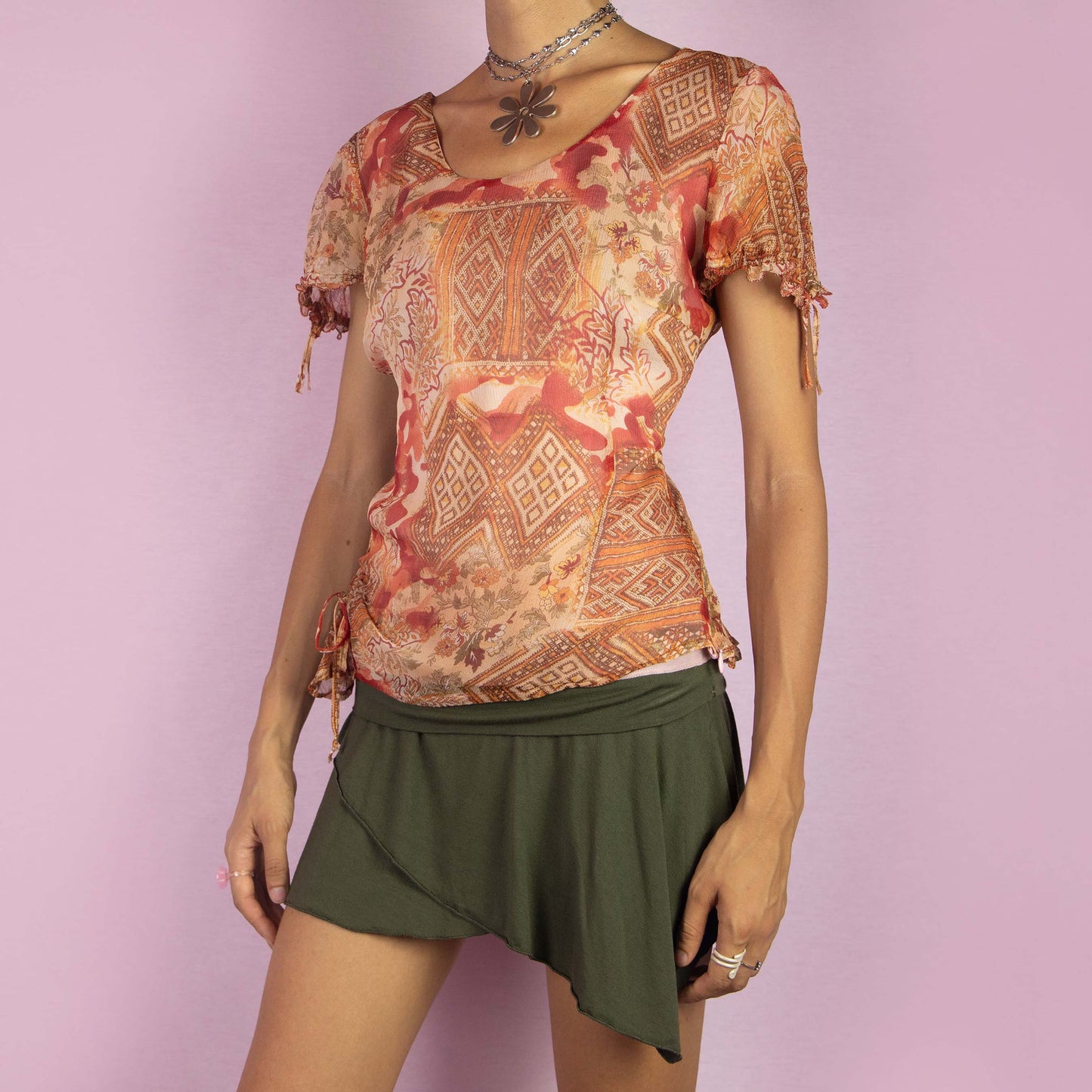 The Y2K Abstract Sheer Top is a vintage 2000s blouse featuring a warm-toned abstract print in orange, red and beige hues. Designed with a semi-sheer fabric overlay, short sleeves, adjustable side ruching with ties for a customized fit and a side zipper closure. Perfect for casual summer outings or adding a touch of boho flair to your wardrobe.