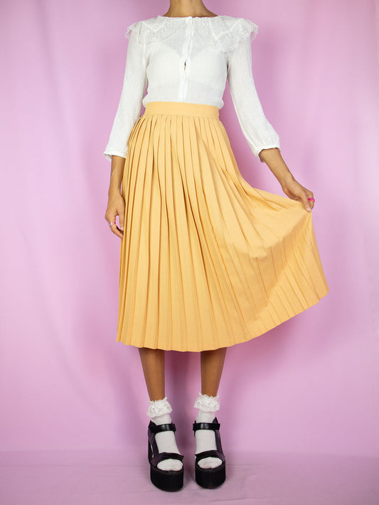 The Vintage 80's Orange Pleated Midi Skirt is a pastel light orange pleated skirt with a back zipper closure. A classic retro preppy uniform-style skirt from the 1980s.