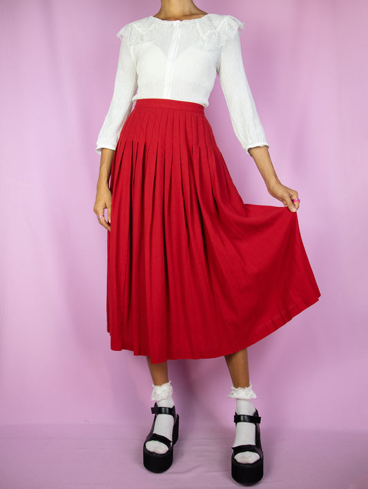 The Vintage 80's Red Wool Pleated Skirt is a pleated midi skirt made of pure new wool in a vibrant red hue, featuring a side button closure. A gorgeous classic retro preppy uniform-style skirt from the 1980s.