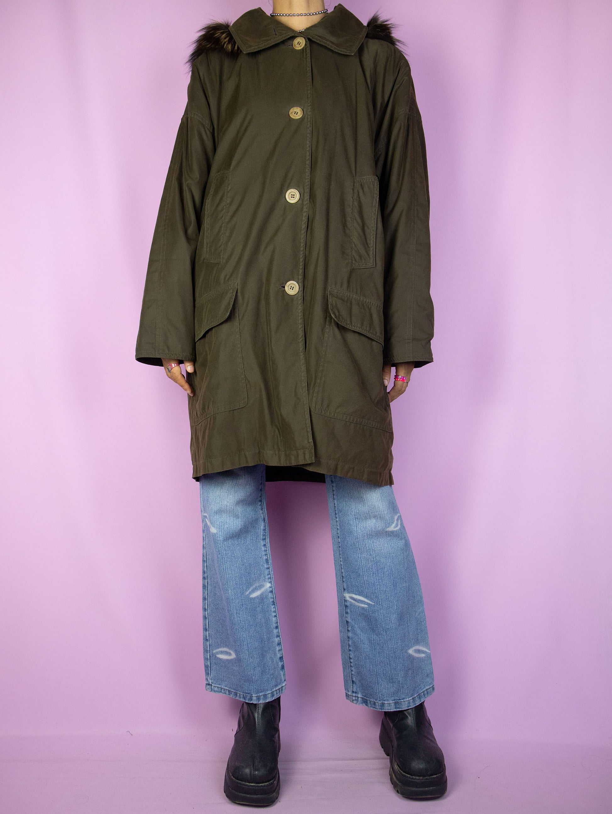 The Vintage 90's Dark Green Parka Jacket is a dark greenish-brown coat with pockets, buttons, and a removable hood with fur. A classic retro grunge winter coat from the 1990s.