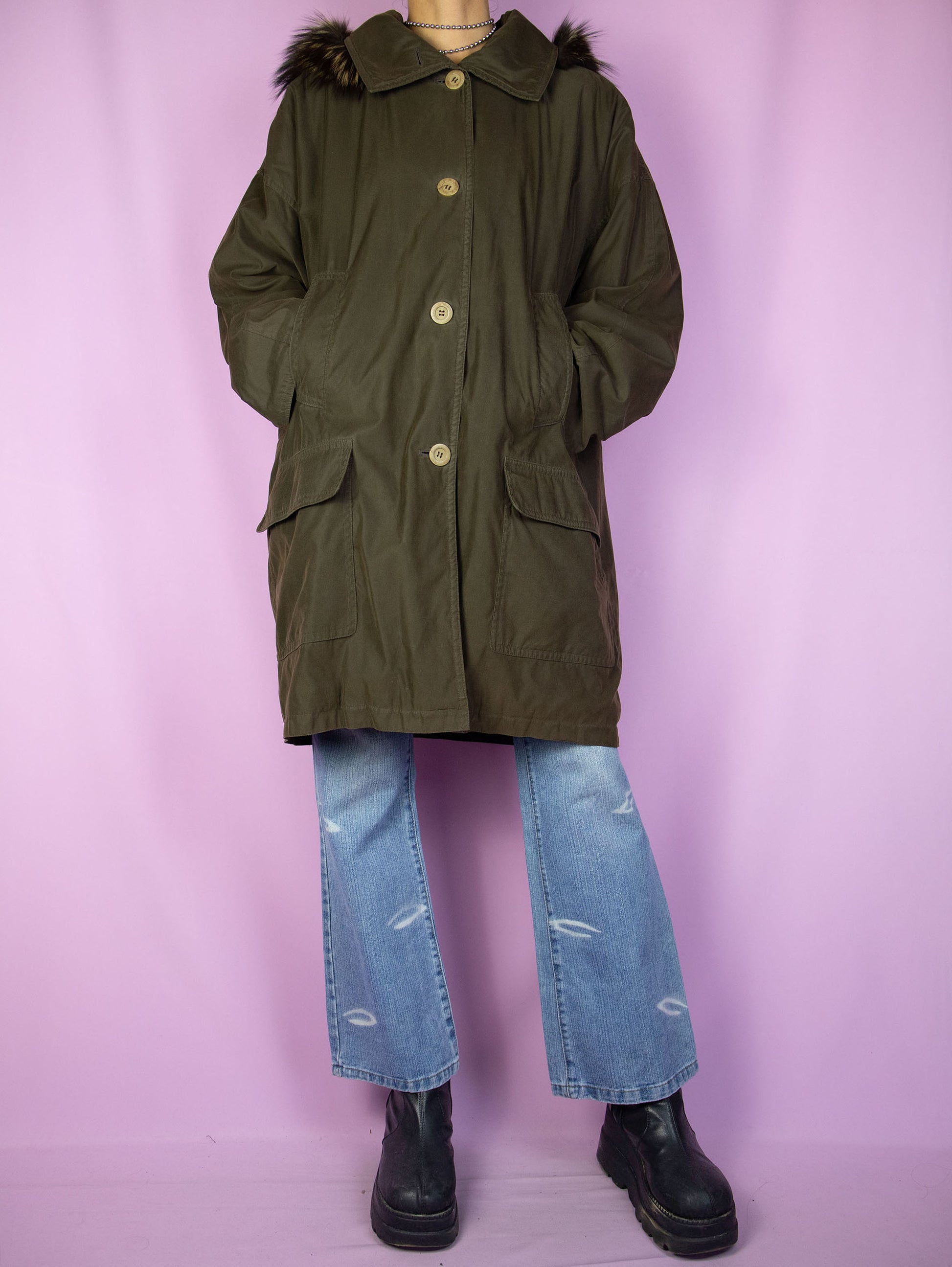 The Vintage 90's Dark Green Parka Jacket is a dark greenish-brown coat with pockets, buttons, and a removable hood with fur. A classic retro grunge winter coat from the 1990s.