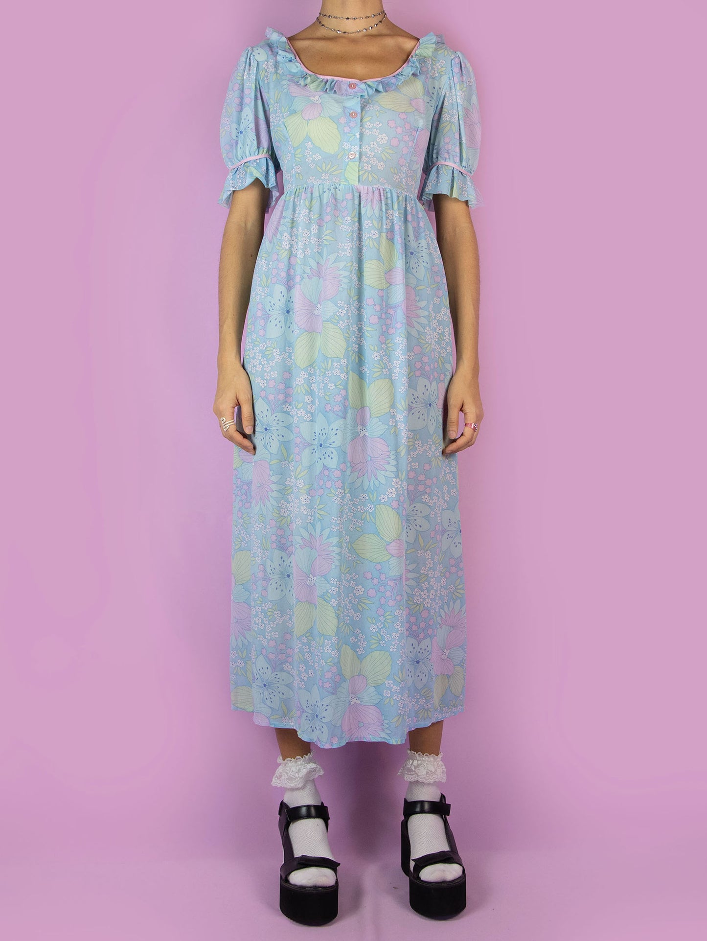 The Vintage 70s Floral Puff Sleeve Prairie Dress is a blue semi-sheer maxi dress in a multicolored floral pattern with short puff sleeves, ruffles, and buttons at the front. Country western inspired 1970s boho midi dress.