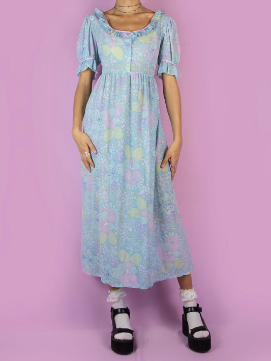 The Vintage 70s Floral Puff Sleeve Prairie Dress is a blue semi-sheer maxi dress in a multicolored floral pattern with short puff sleeves, ruffles, and buttons at the front. Country western inspired 1970s boho midi dress.