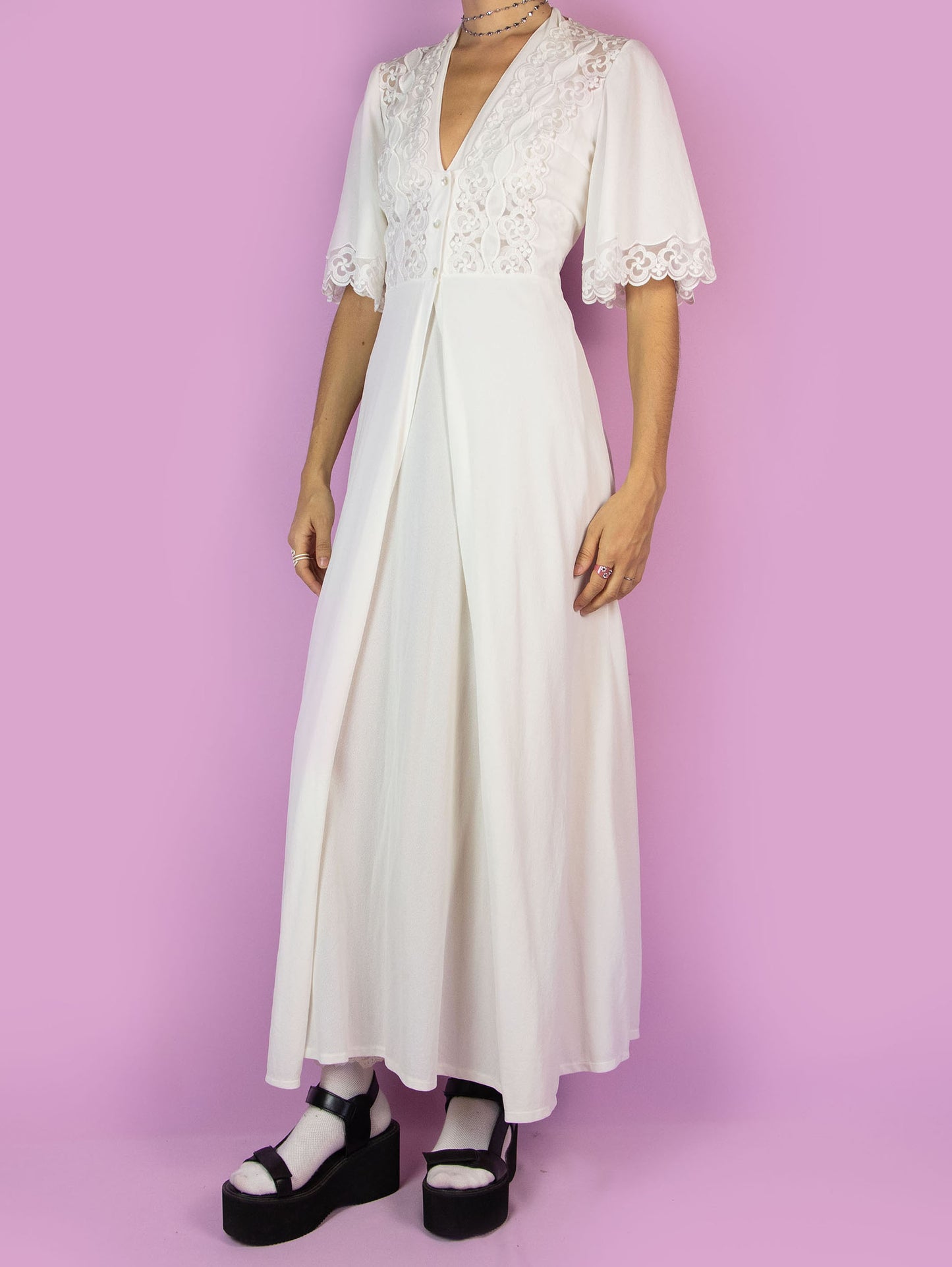 The Vintage 70s White Lace Duster Robe is a long maxi white robe with short sleeves, lace details, and a button closure at the front. Romantic 1970s boho peignoir jacket.