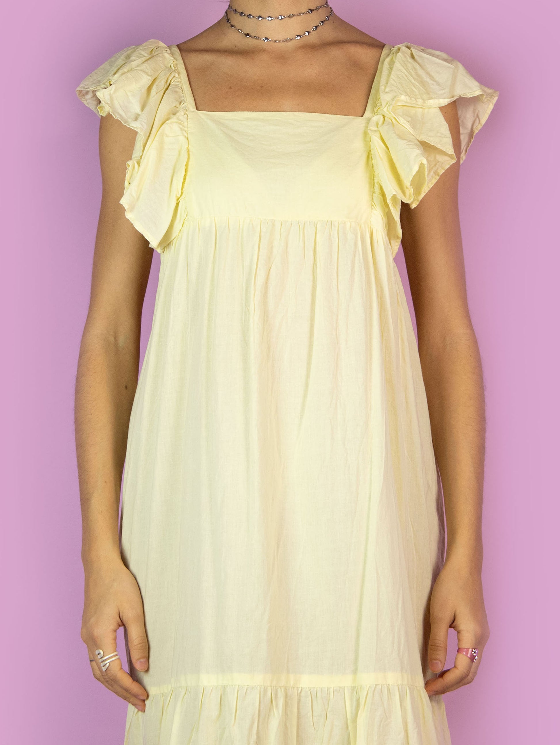 The Y2K Boho Tiered Midi Dress is a vintage light pastel yellow dress with a slightly transparent tiered design and ruffles on the straps. Summer 2000s beach cover up maxi dress.