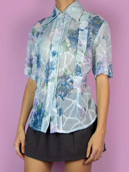 The Y2K Romantic Blue Sheer Blouse is a vintage light blue floral semi-transparent short-sleeve top with a collar, buttons, and gathered ruffle details. Boho retro 2000s summer shirt.