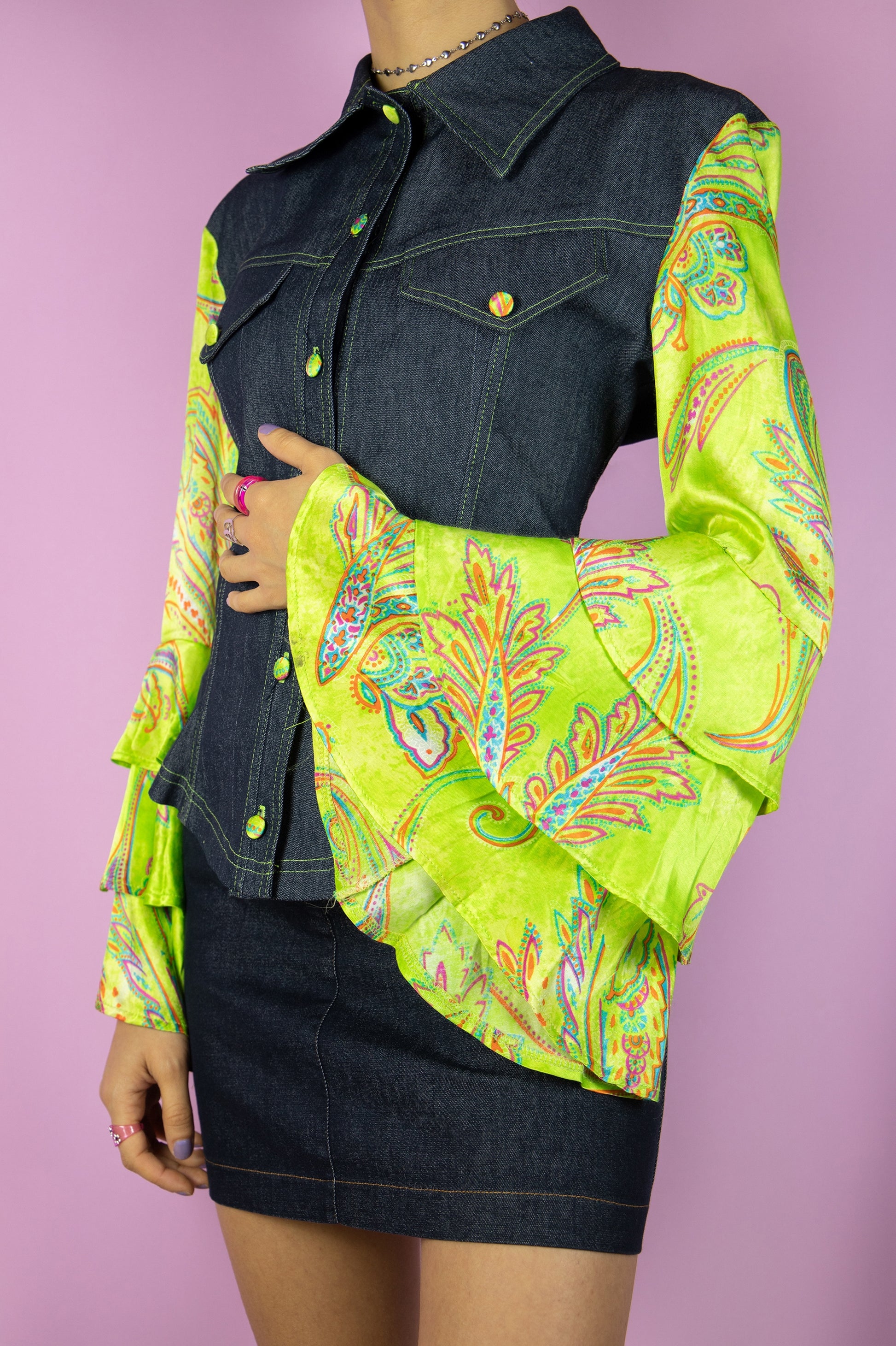 The Vintage Y2K Bell Sleeve Denim Jacket is a dark denim jacket adorned with paisley floral print green bell sleeves, featuring stylish ruffles. This cyber statement jacket hails from the fashion era of the 2000s.