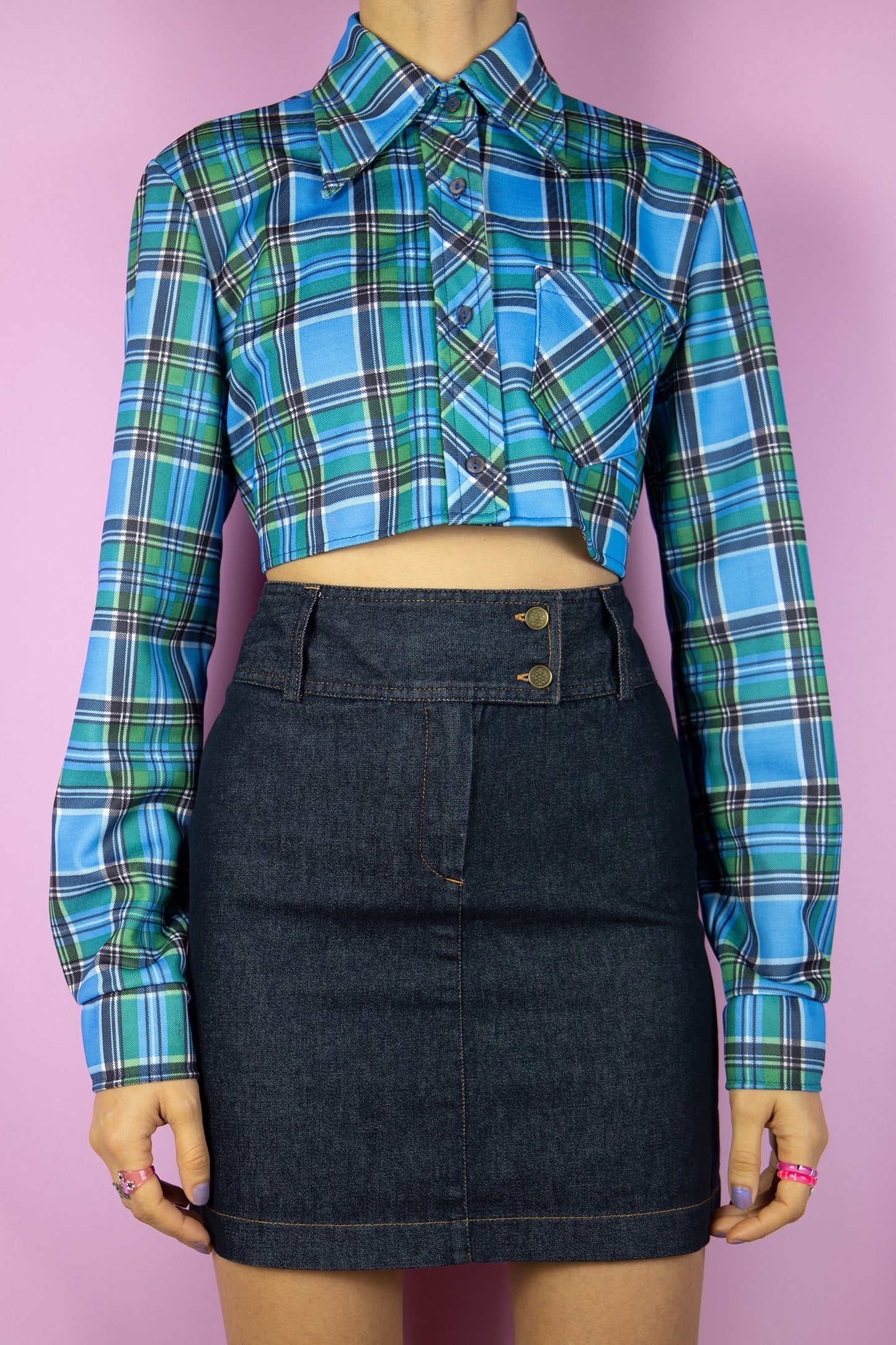 The Vintage 90’s Blue Plaid Cropped Shirt is a long-sleeve top featuring blue and green checkered patterns, a collar, buttons, and a pocket. Its oversized fit adds an extra touch to this stylish utility grunge overshirt from the 1990s.