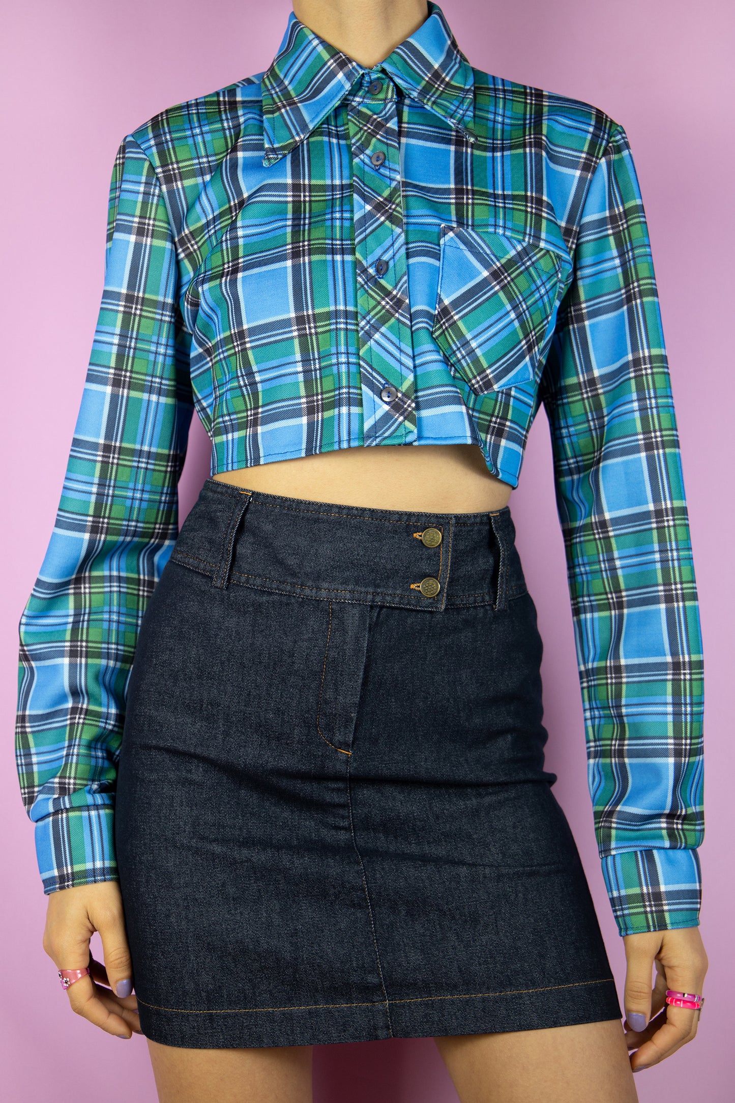 The Vintage 90’s Blue Plaid Cropped Shirt is a long-sleeve top featuring blue and green checkered patterns, a collar, buttons, and a pocket. Its oversized fit adds an extra touch to this stylish utility grunge overshirt from the 1990s.