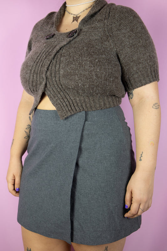 The Vintage Y2K Gray Wrap Mini Skirt is a stylish gray wrap skirt secured with velcro and buttons. An iconic cyber mini skirt circa the 2000s, perfect for wearing at festivals, raves, and clubbing.